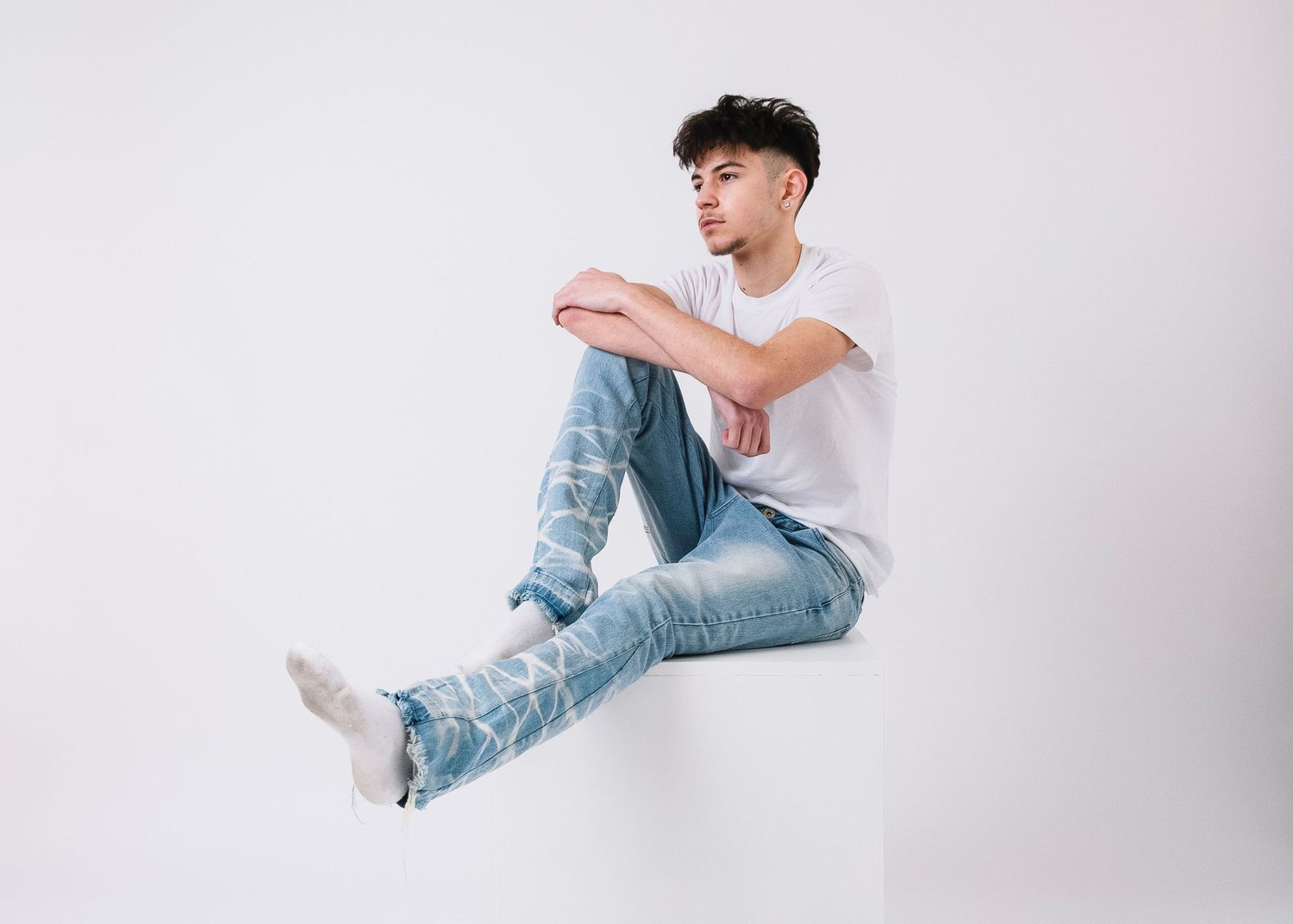 Young person in casual attire sitting against white background in artistic poses.