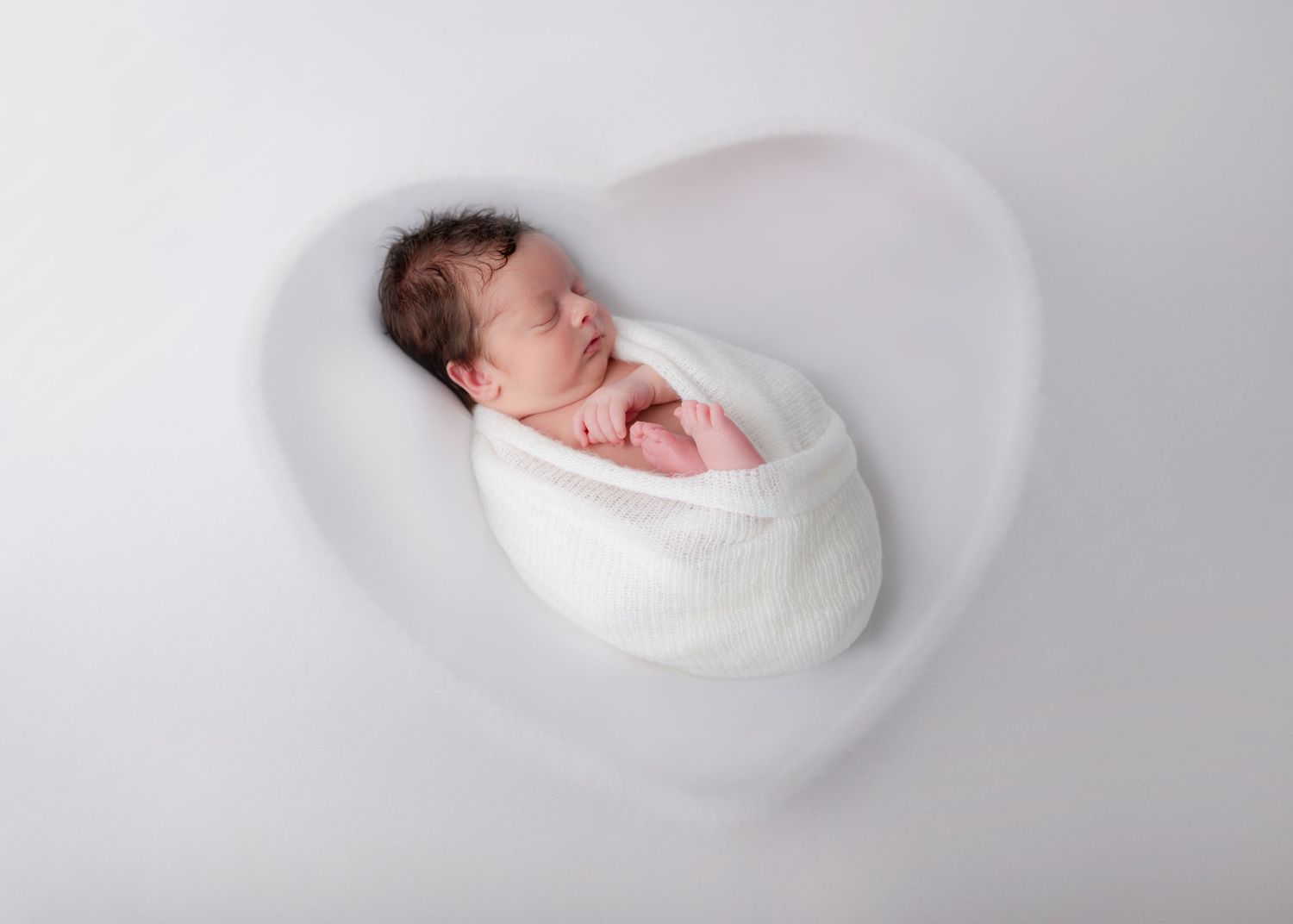 Artistic newborn photography of sleeping baby wrapped in white against light background.