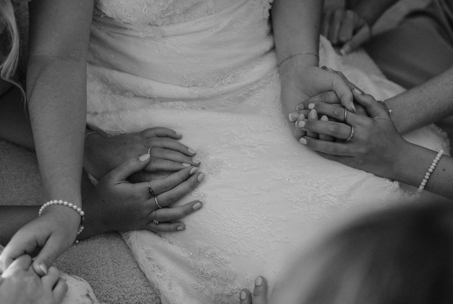Close-up detail of hands resting on a white wedding dress.