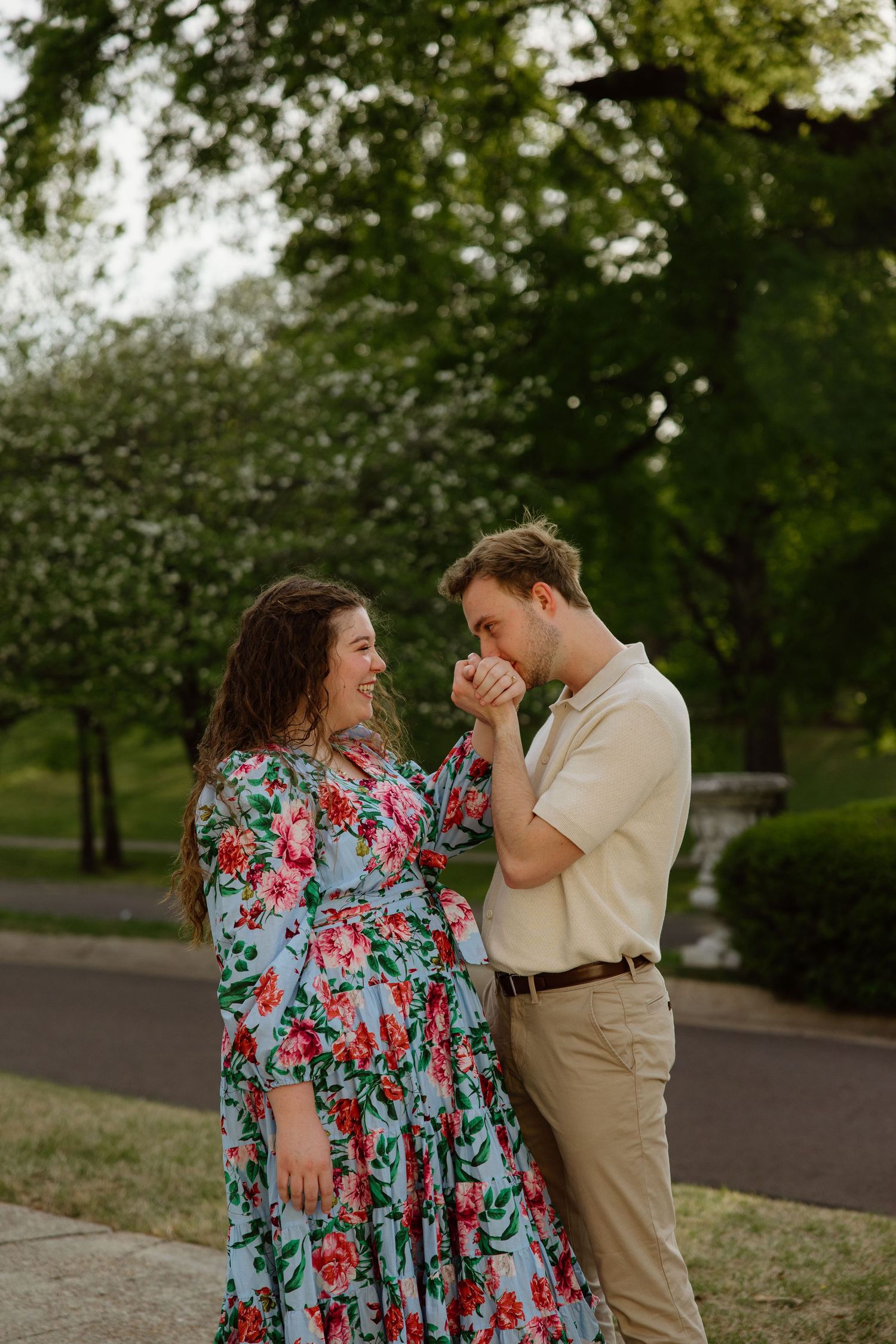 Romantic moment between couple in floral dress and khakis on a tree-lined path.