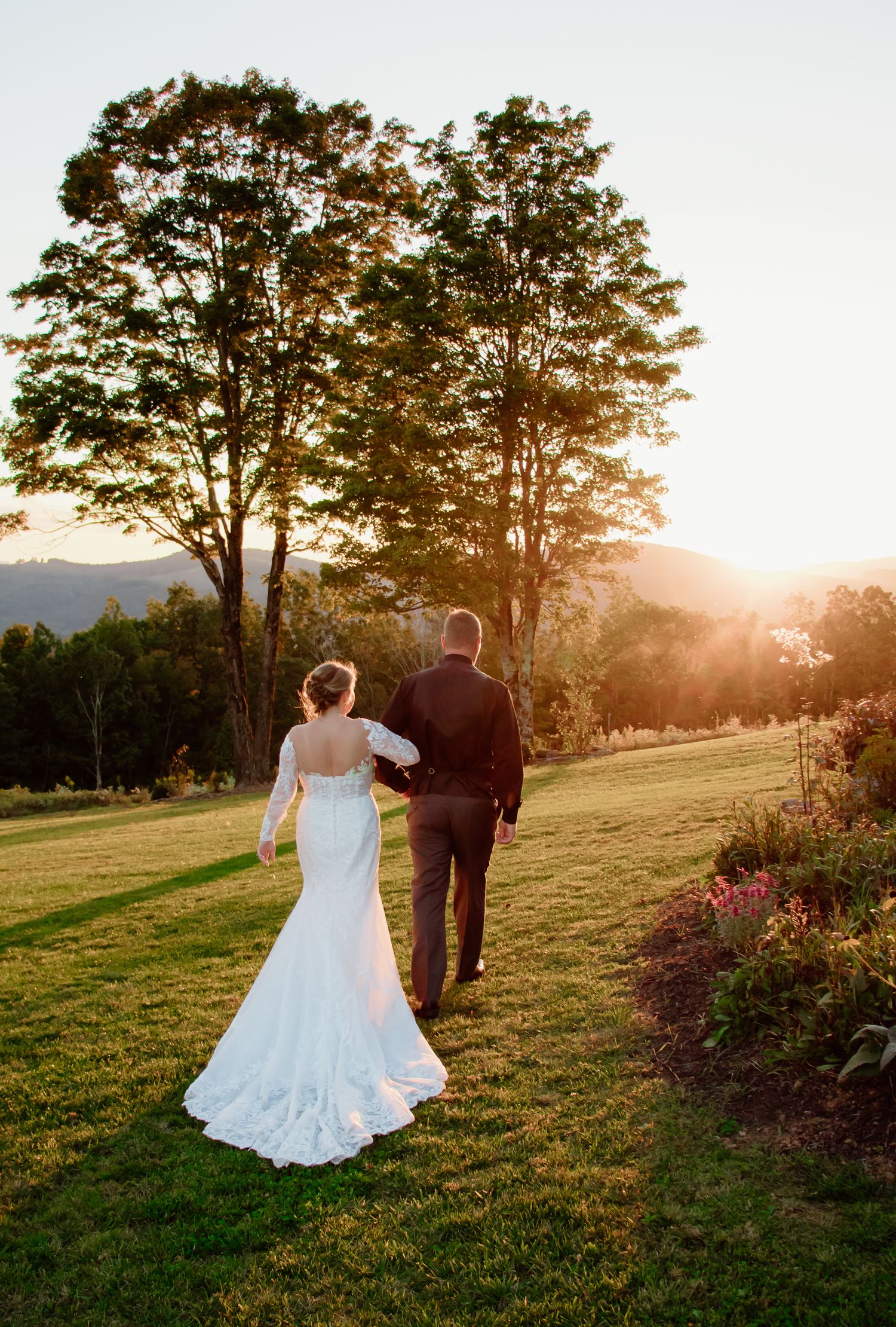 A couple walks away into the sunset on their wedding day with mountains in the background.