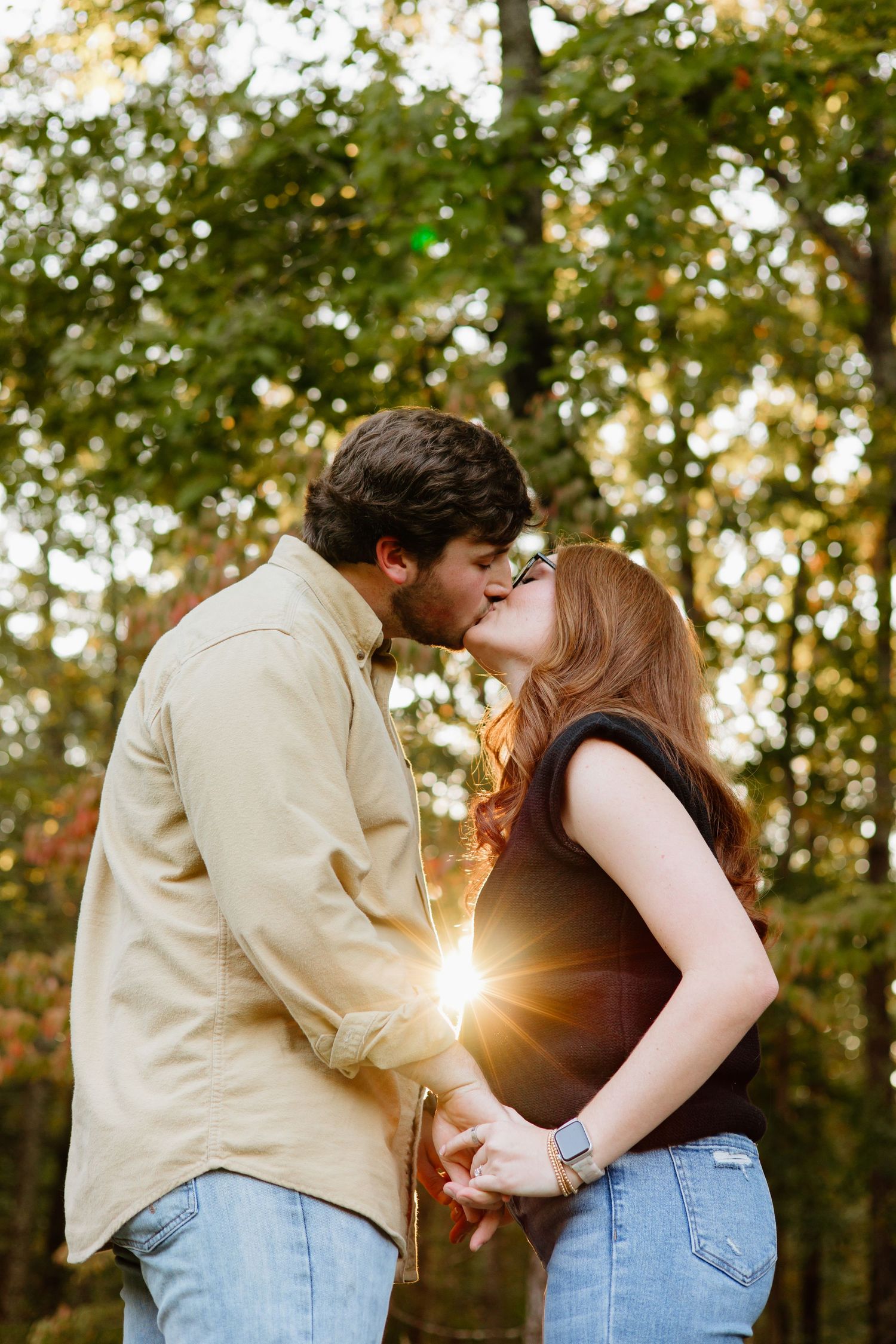 Romantic sunset kiss between couple with sunburst through trees.
