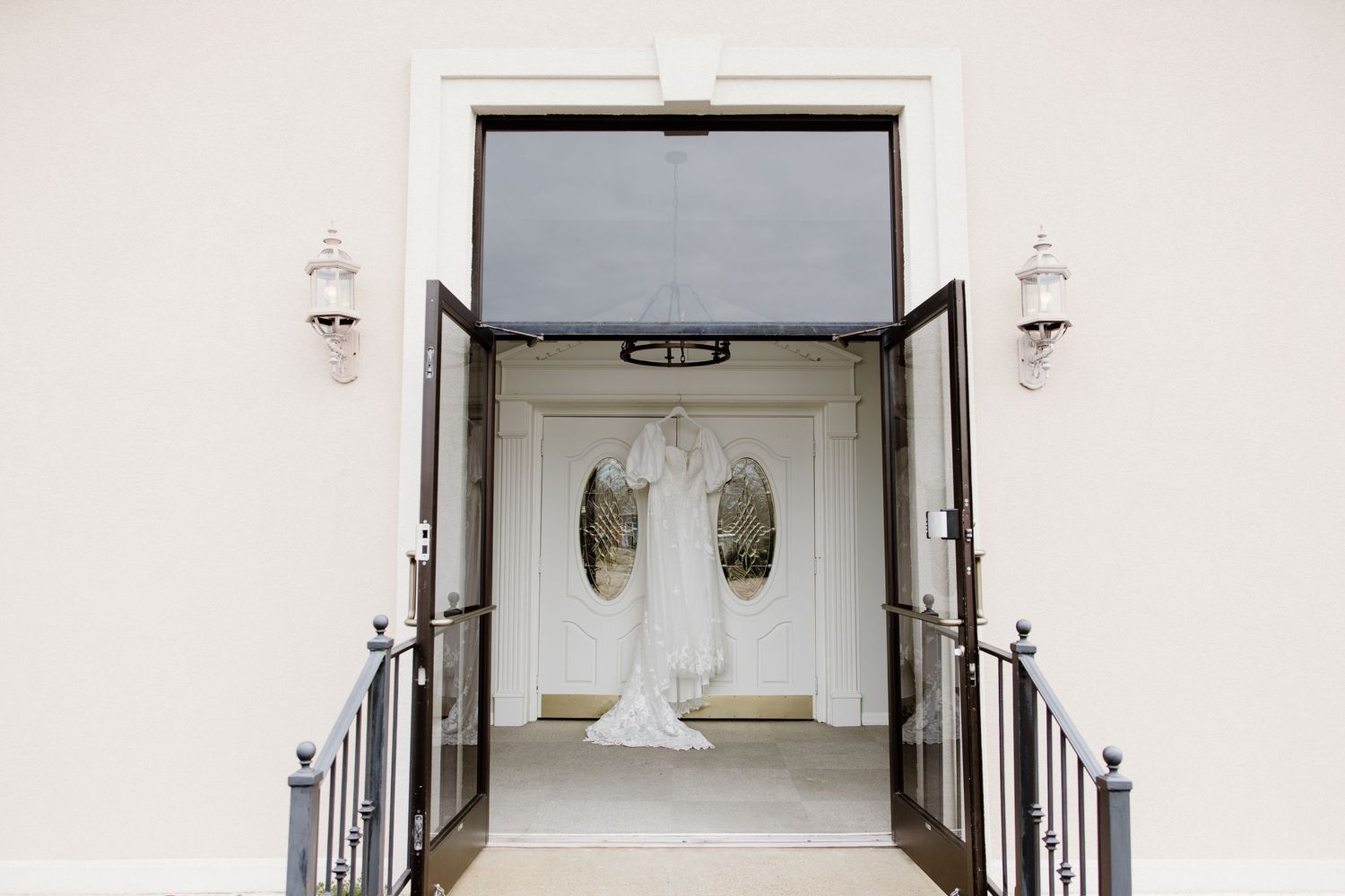 Wedding dress hanging in doorway of white building entrance with symmetrical design.