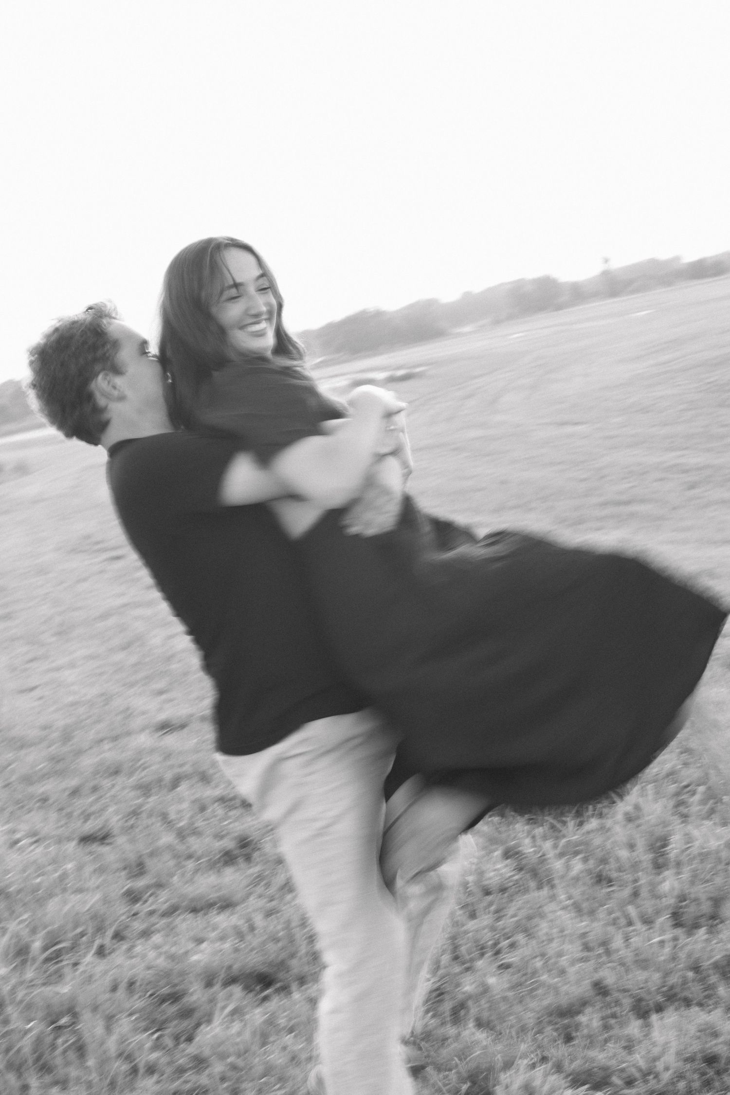 Black and white photo of couple in joyful embrace spinning outdoors.