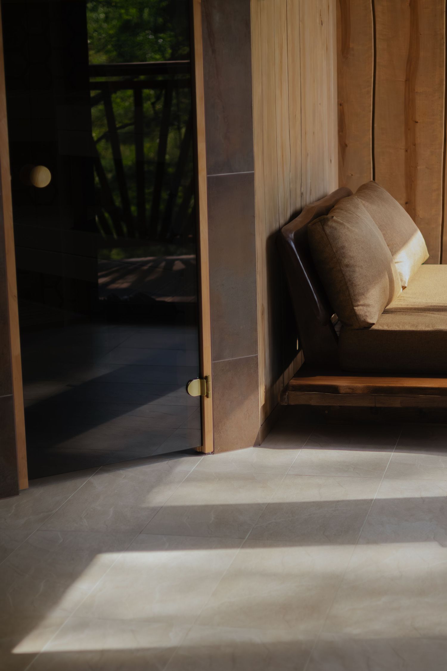 Sunlight casts dramatic shadows across a minimalist interior space with wooden walls and a concrete floor.