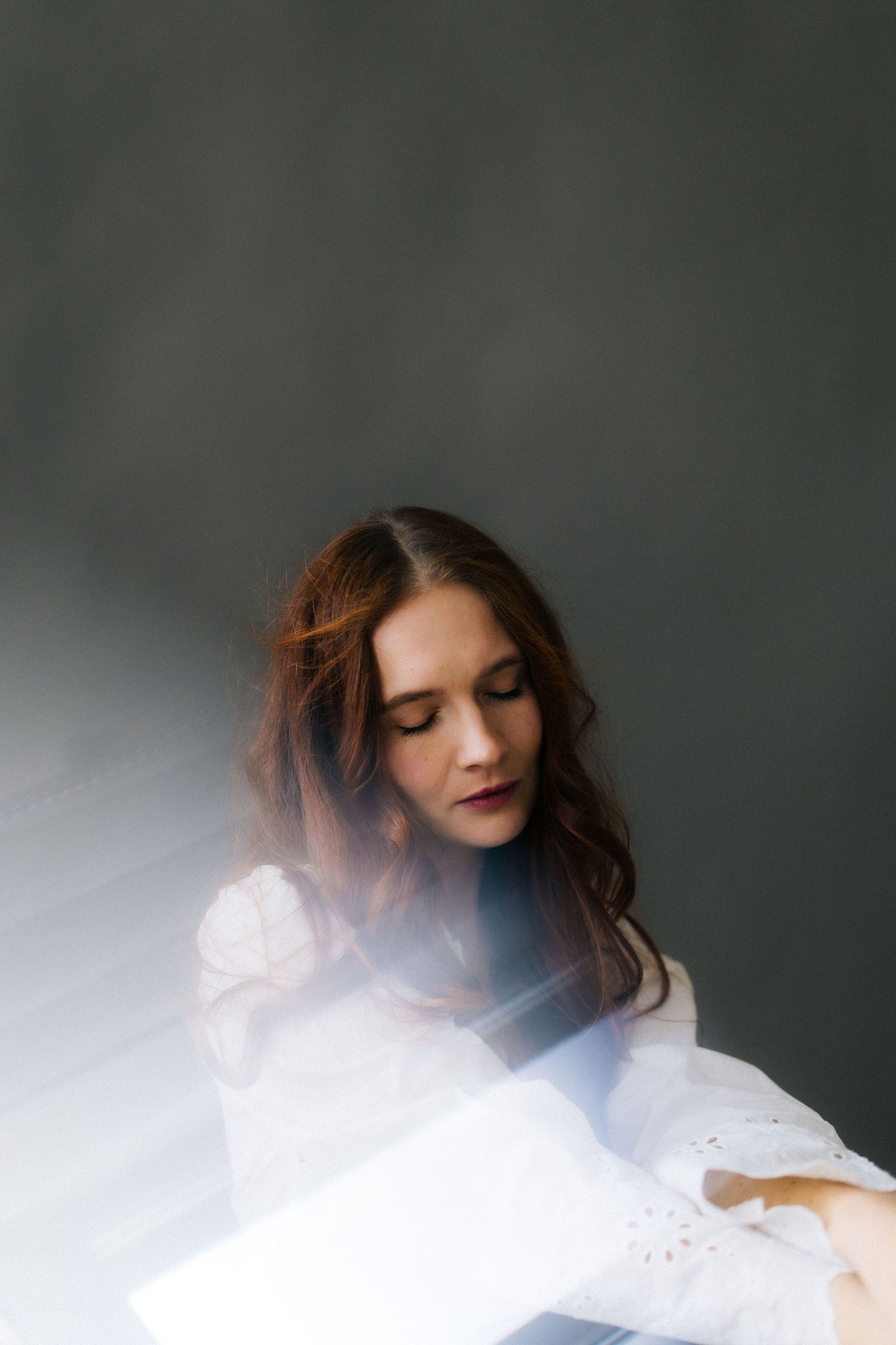 Ethereal portrait of someone in a white dress against a dark background with soft, dreamy lighting effects.