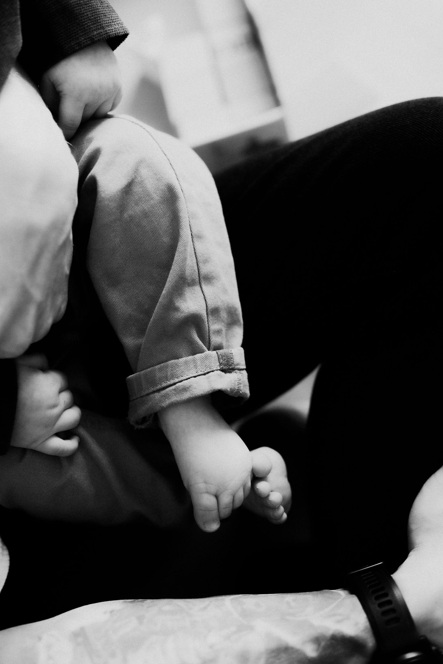 Close up black and white image of a small baby foot resting on someone's lap.