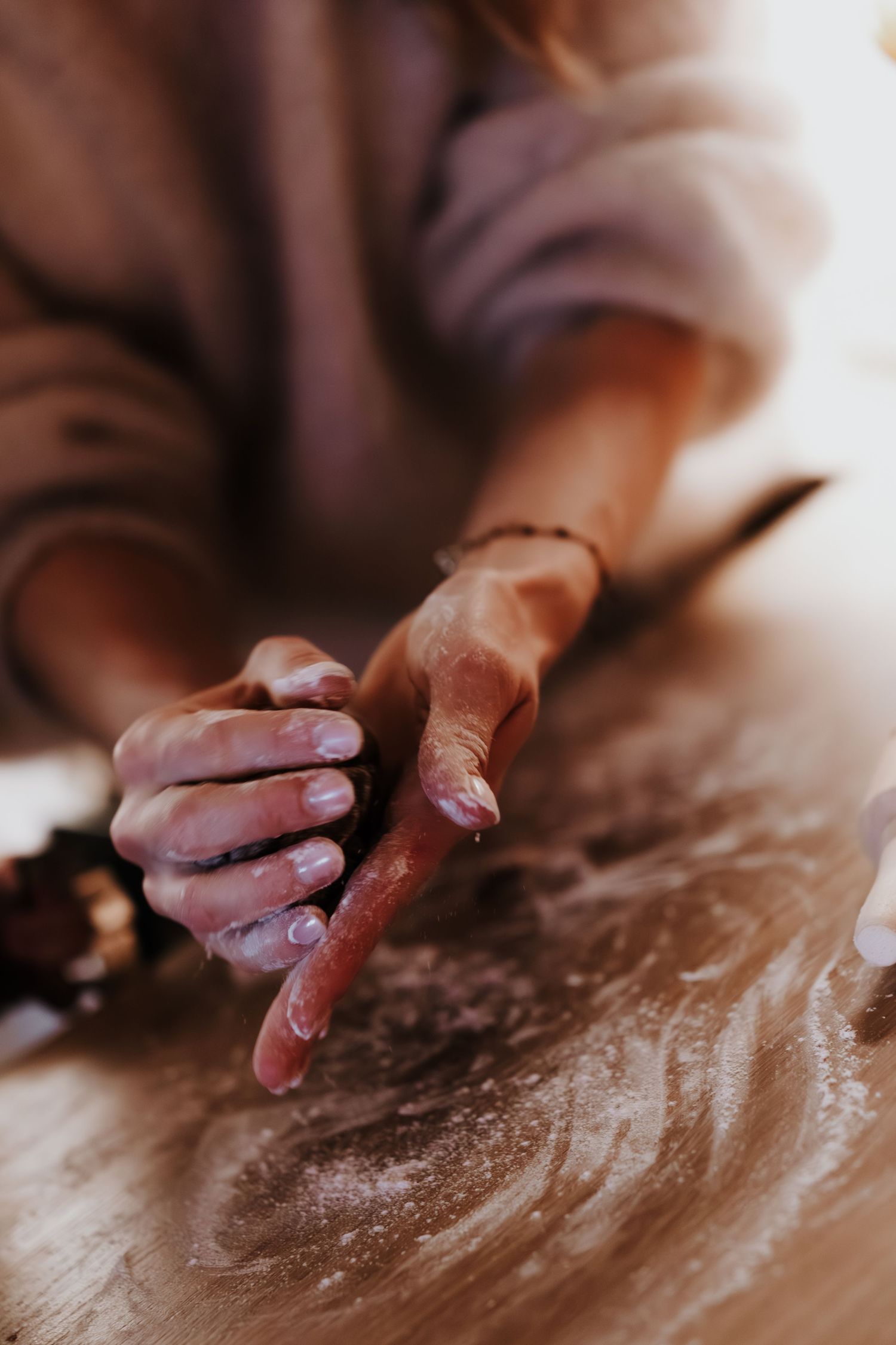 Flour-covered hands kneading dough on a wooden surface in soft, natural lighting.