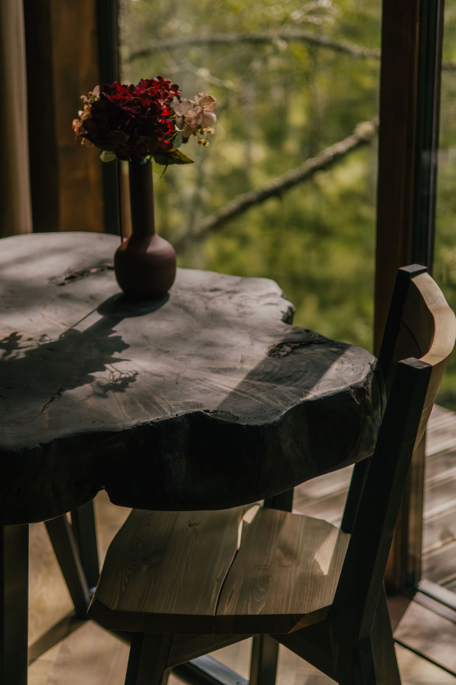 Dark rustic wooden table with multiple sections shown in moody lighting with green foliage visible through window.