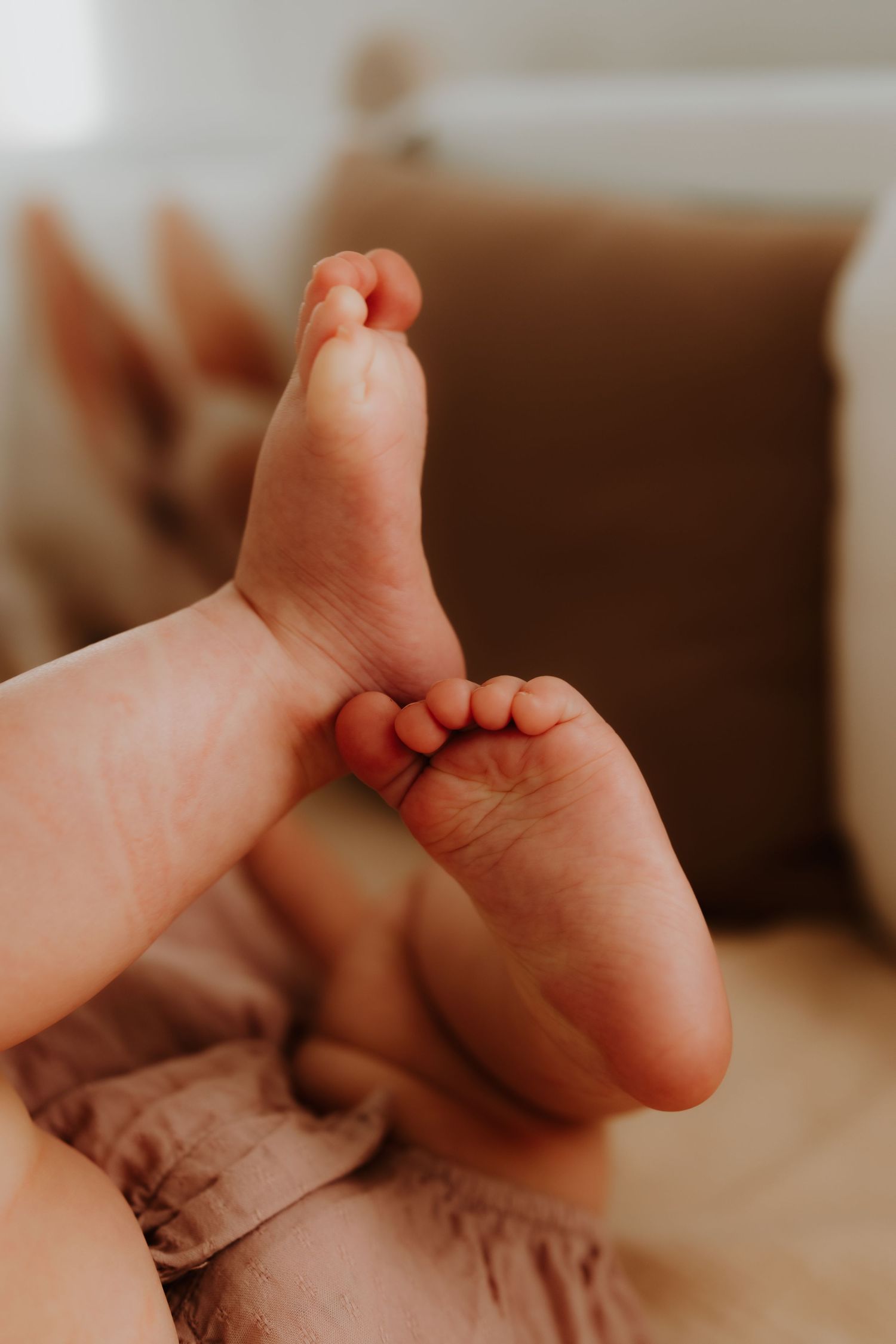 Close-up photo of tiny baby feet with curled toes against a soft brown background in warm lighting.