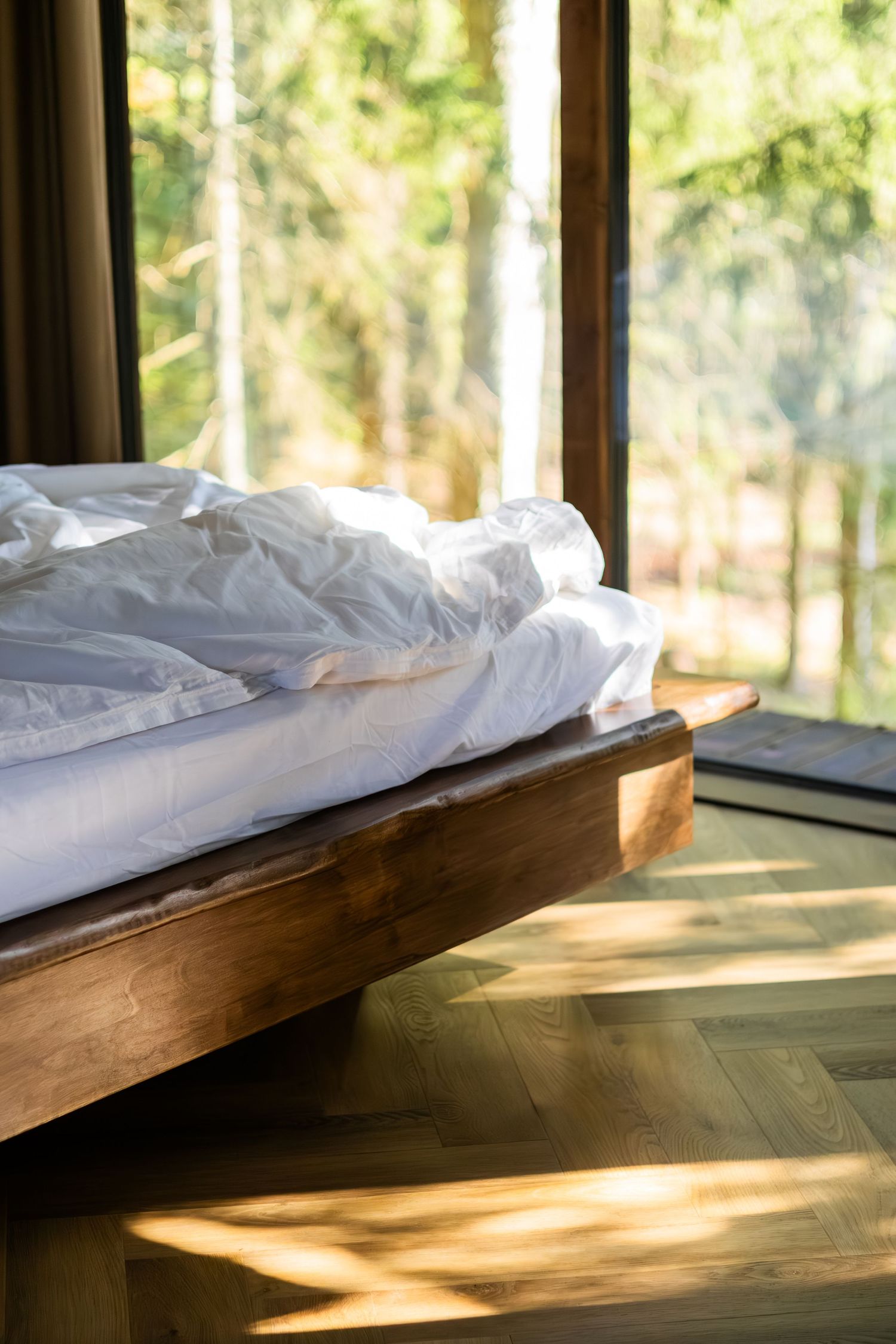Sunlight streams through windows onto a minimalist wooden platform bed with white bedding.