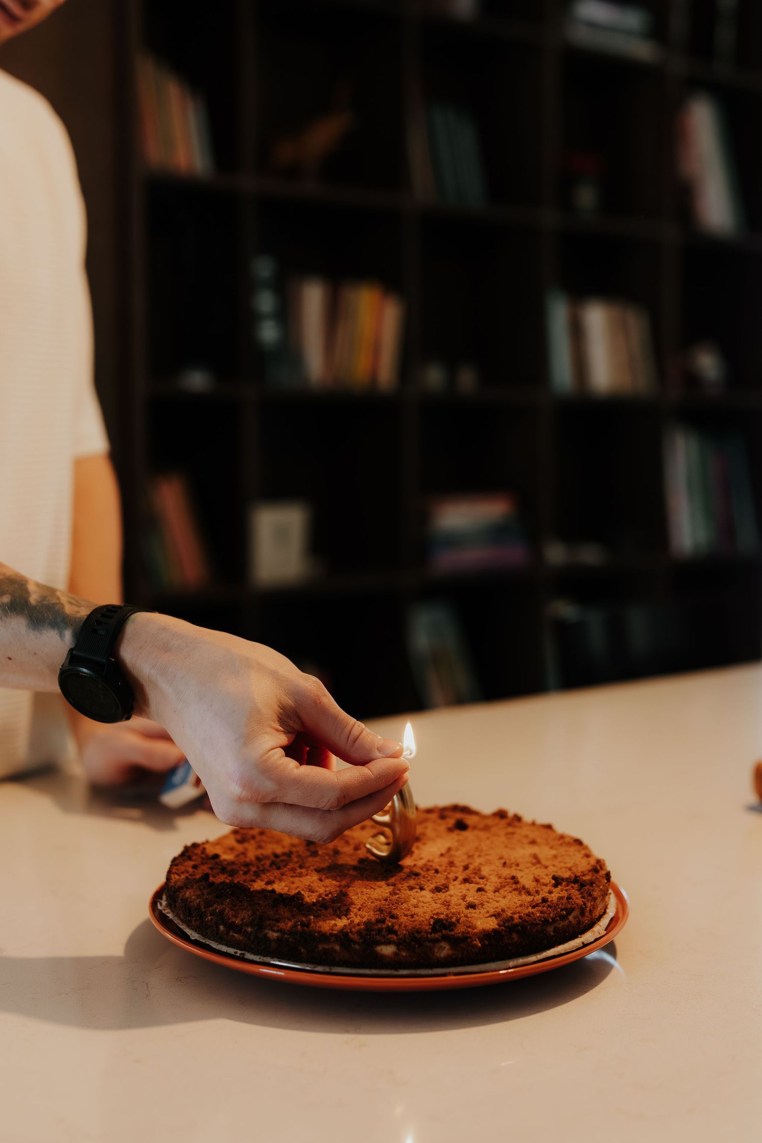 Hands cutting into a freshly baked rustic fruit tart on a white plate against a dark background with bookshelves.