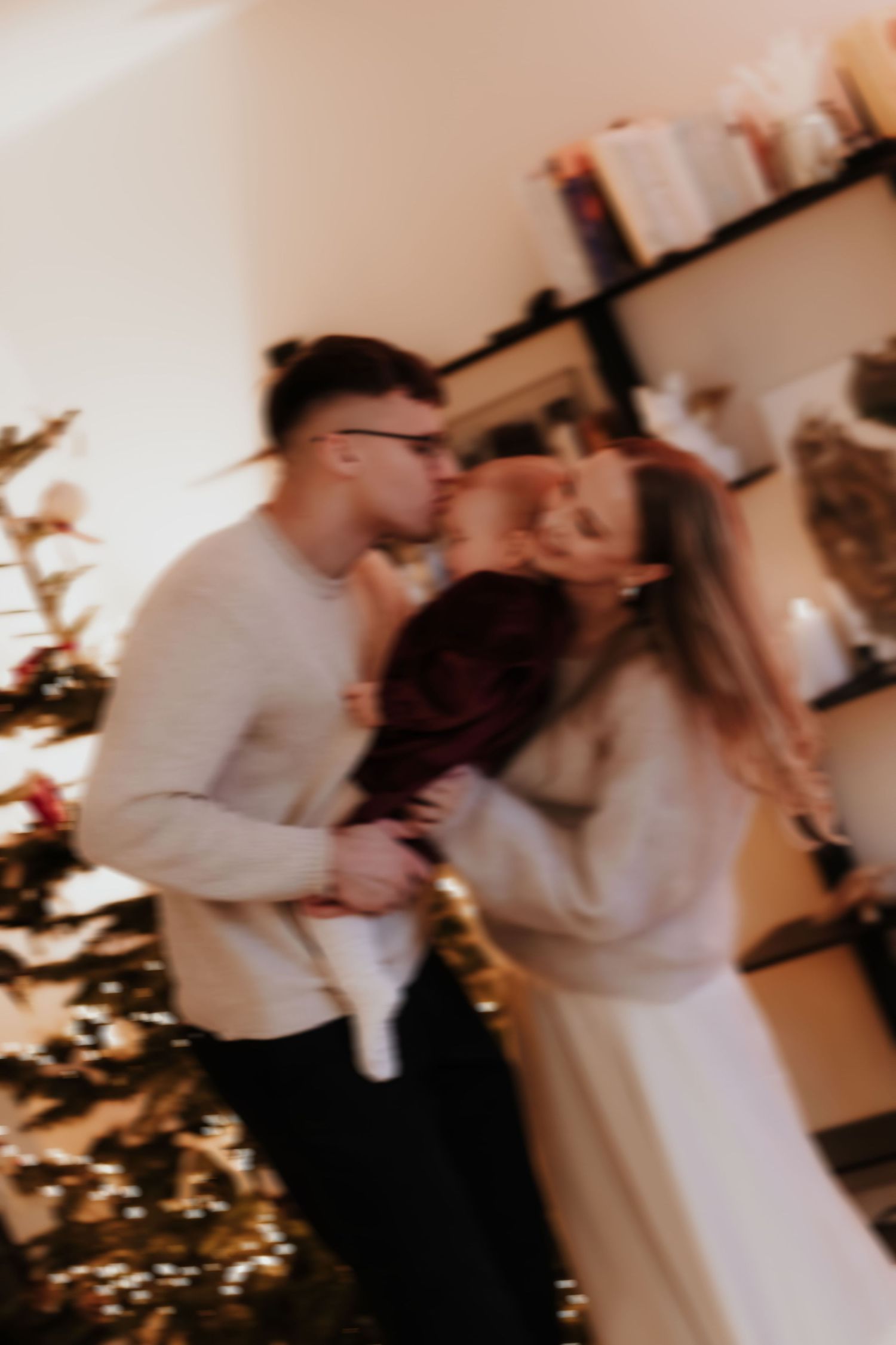 A couple shares a romantic kiss in front of a decorated Christmas tree with warm lighting creating a cozy holiday atmosphere.