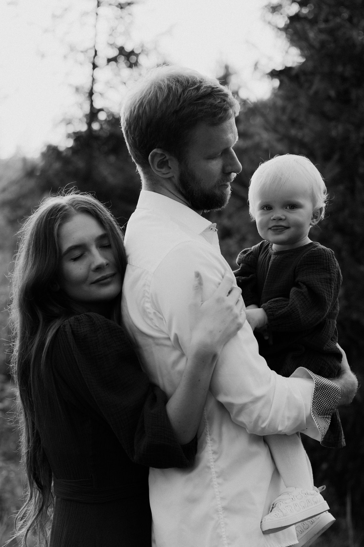 A black and white photo series shows tender family moments between parents and child outdoors.