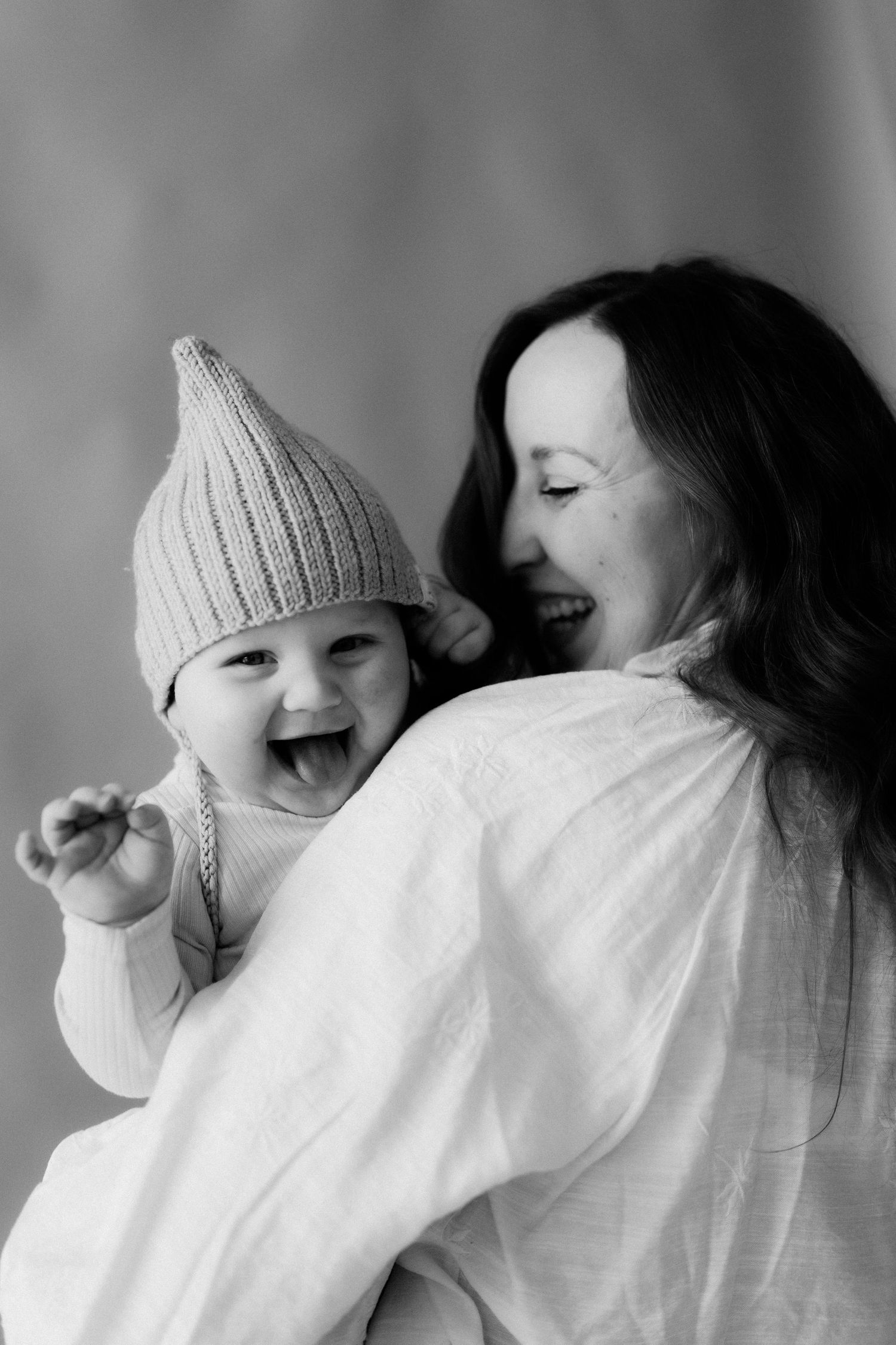 A black and white series of four photos showing someone in a white knit hat laughing while covering their face.