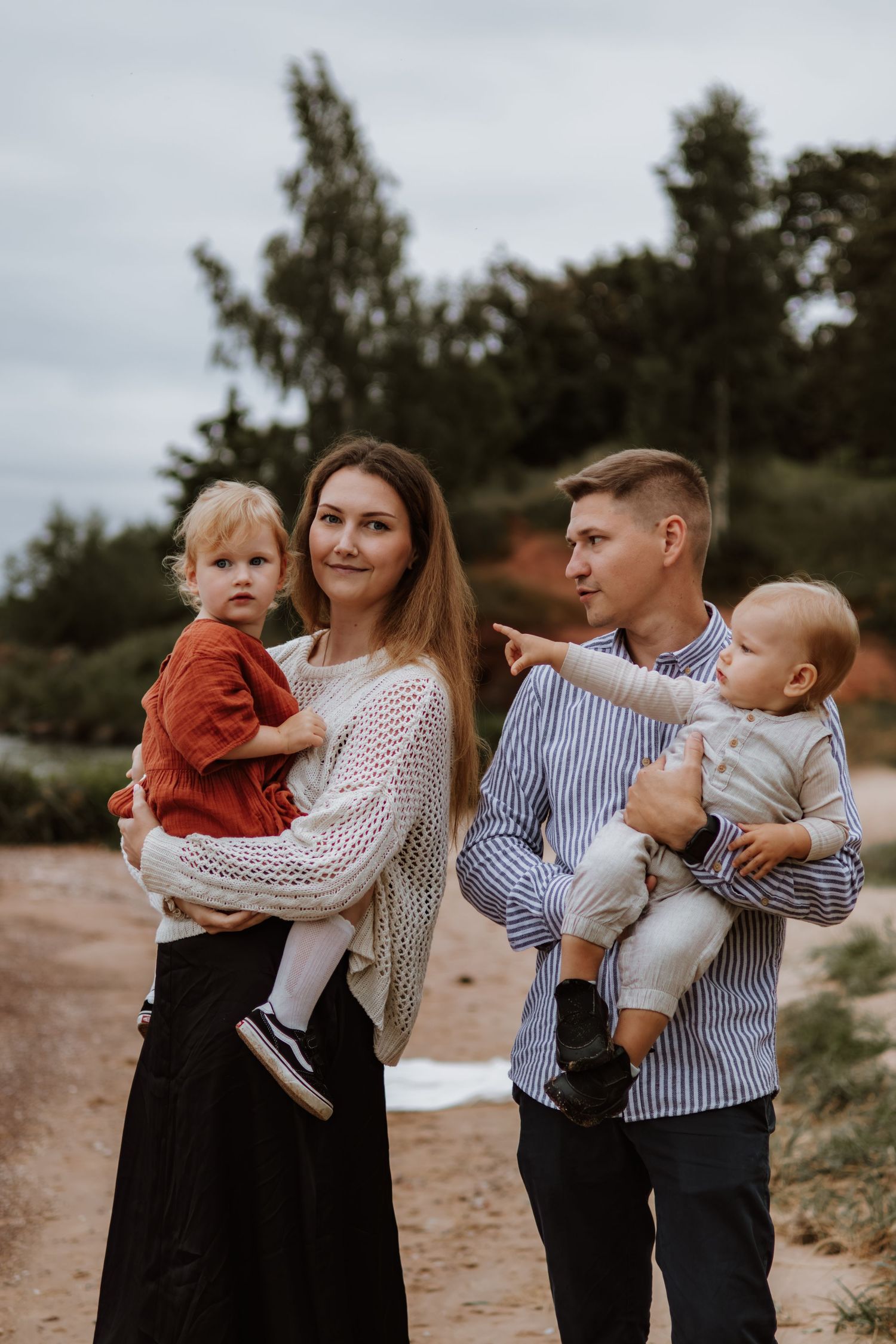 A family in coordinated outfits shares tender moments together on a cloudy day outdoors.