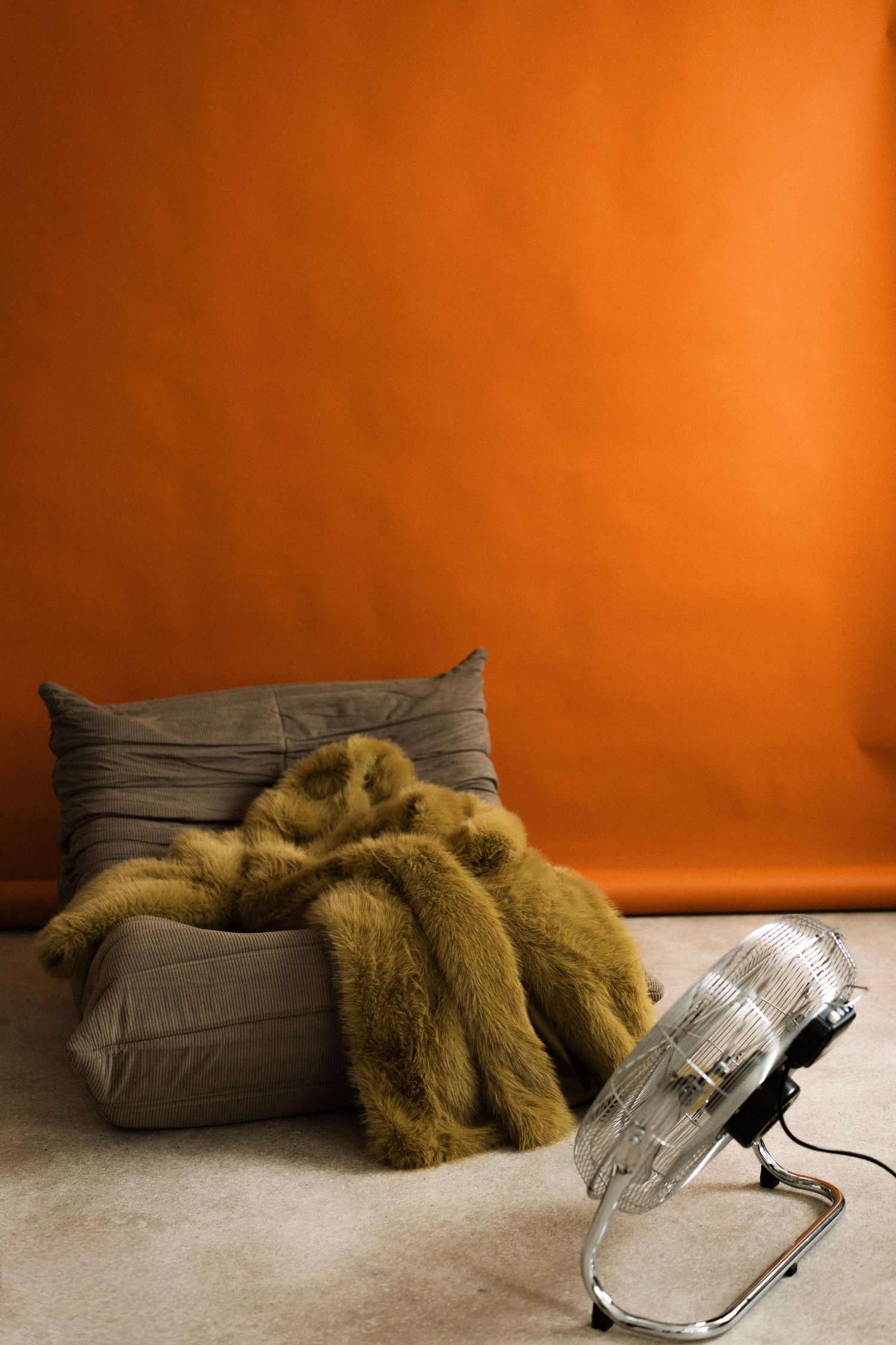 A clear glass computer mouse sits beside a brown pillow and olive-colored throw blanket against an orange background.