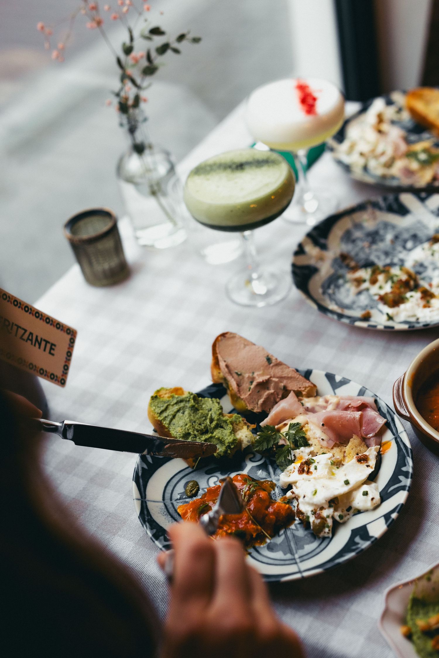 A sequence of elegant plated dishes and cocktails being served at a restaurant table with white linens.