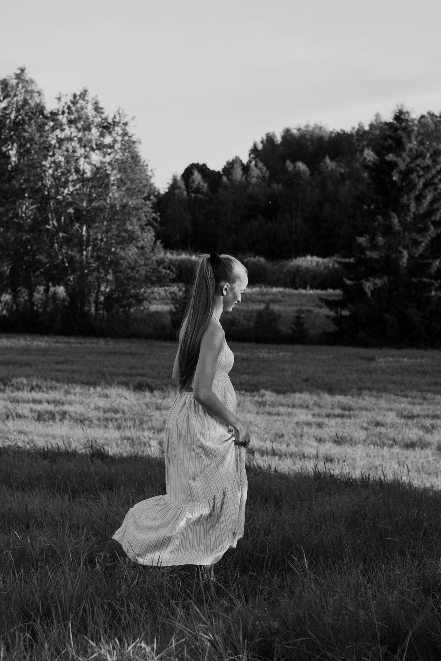 A person in a flowing white dress dances gracefully in a meadow at dusk creating an ethereal black and white scene.