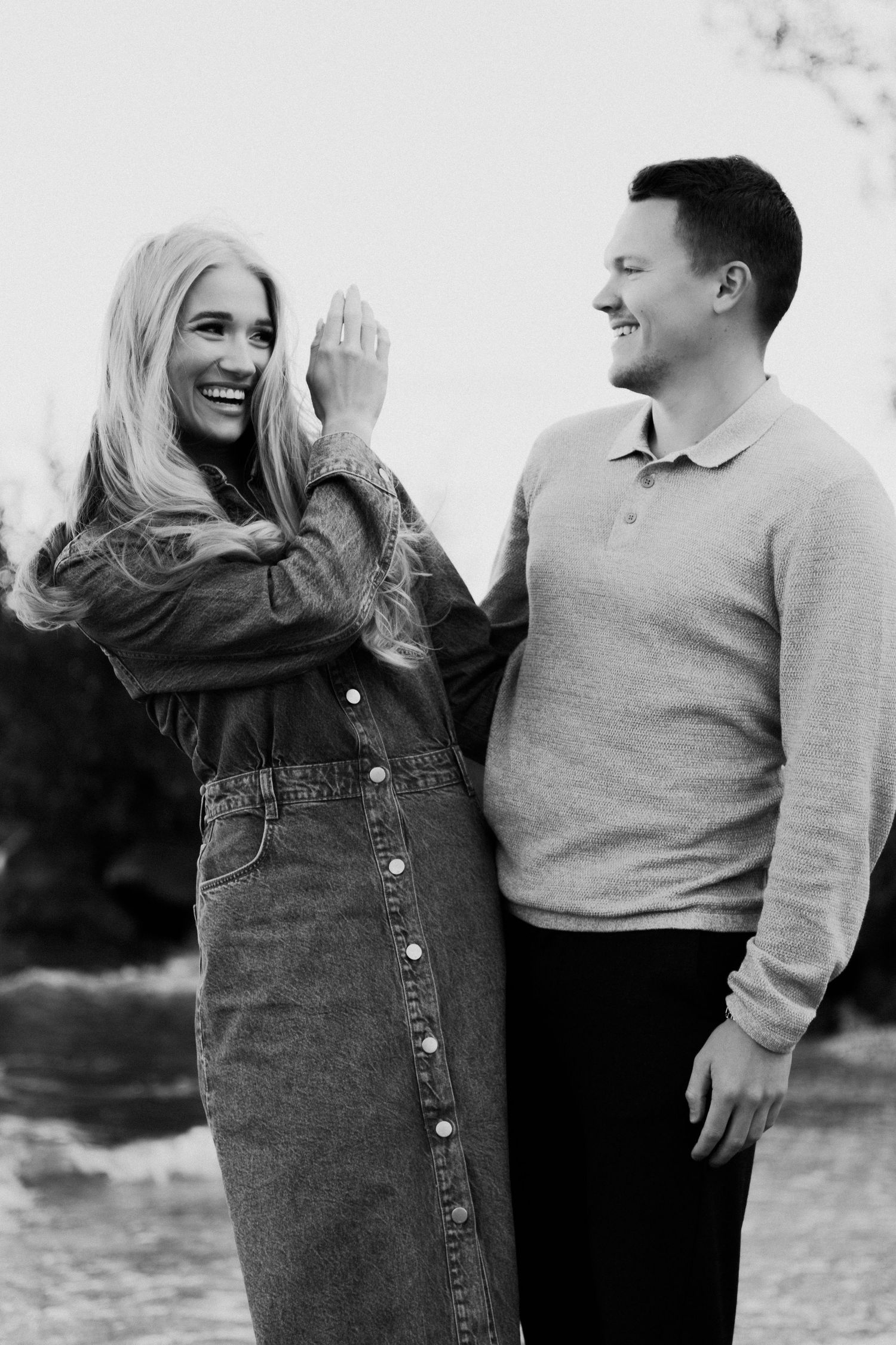 A couple shares candid laughter and joy during a casual outdoor photo session in black and white.