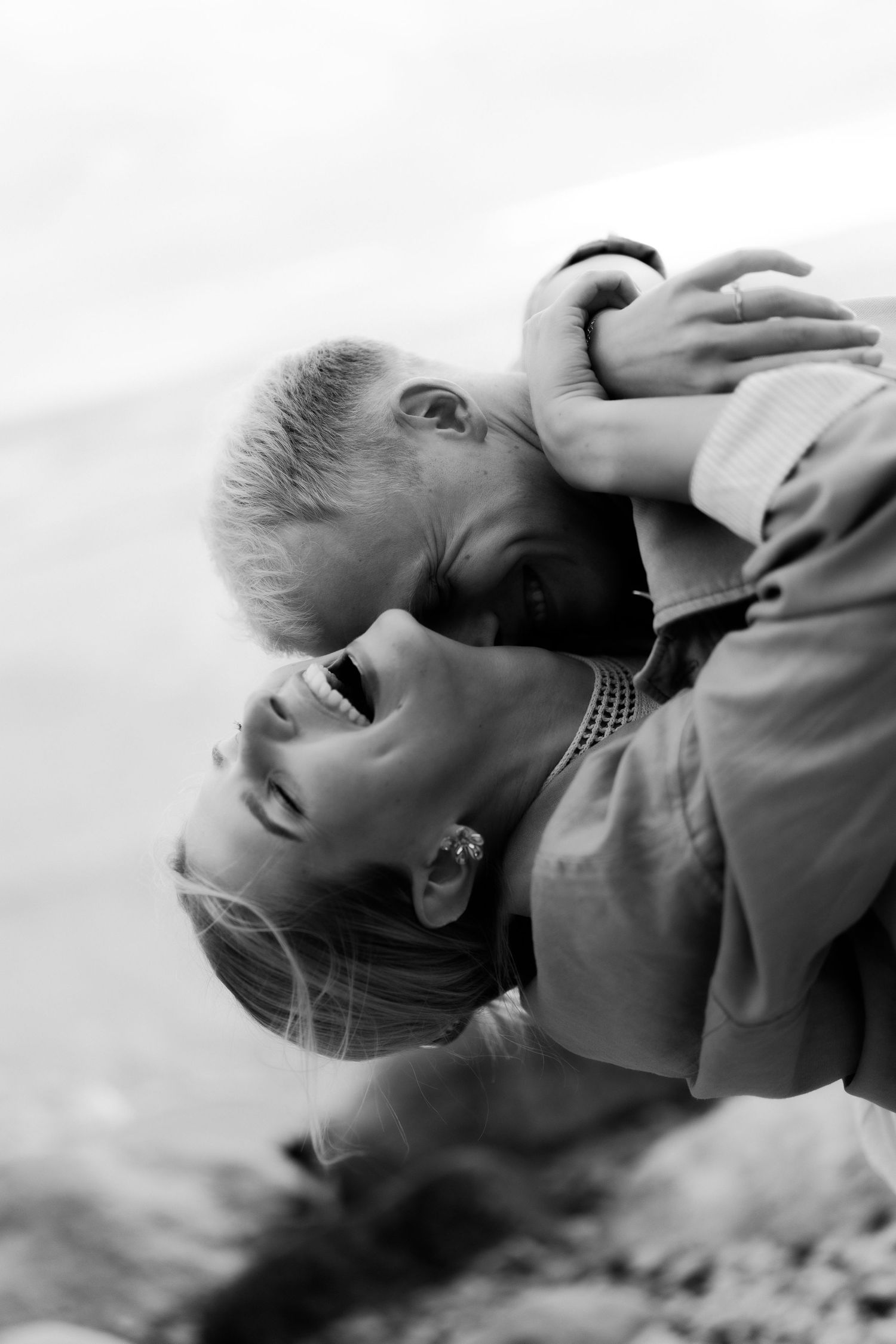 Black and white photo of a couple sharing a romantic moment, woman laughing joyfully as man leans in to kiss her.