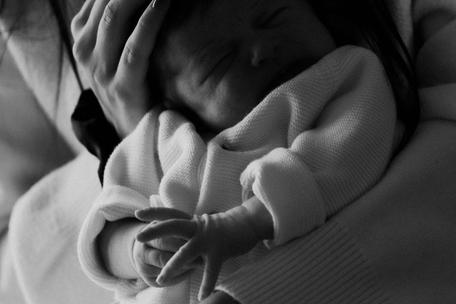 Black and white close-up photograph of hands holding and examining a small baby's feet.