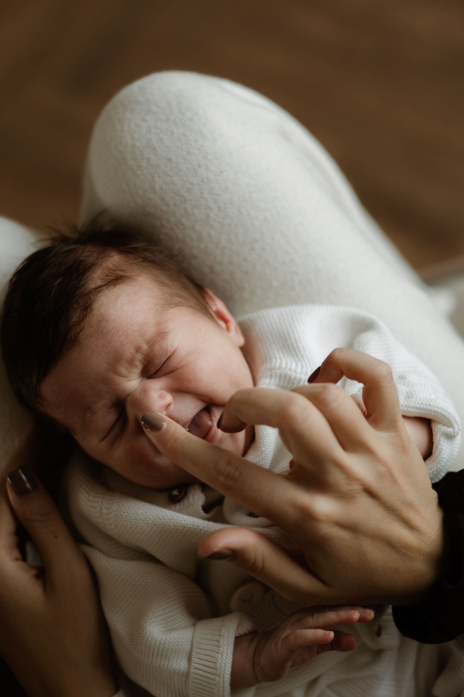 Newborn baby crying while being cradled in a white blanket, with a gentle hand offering comfort.
