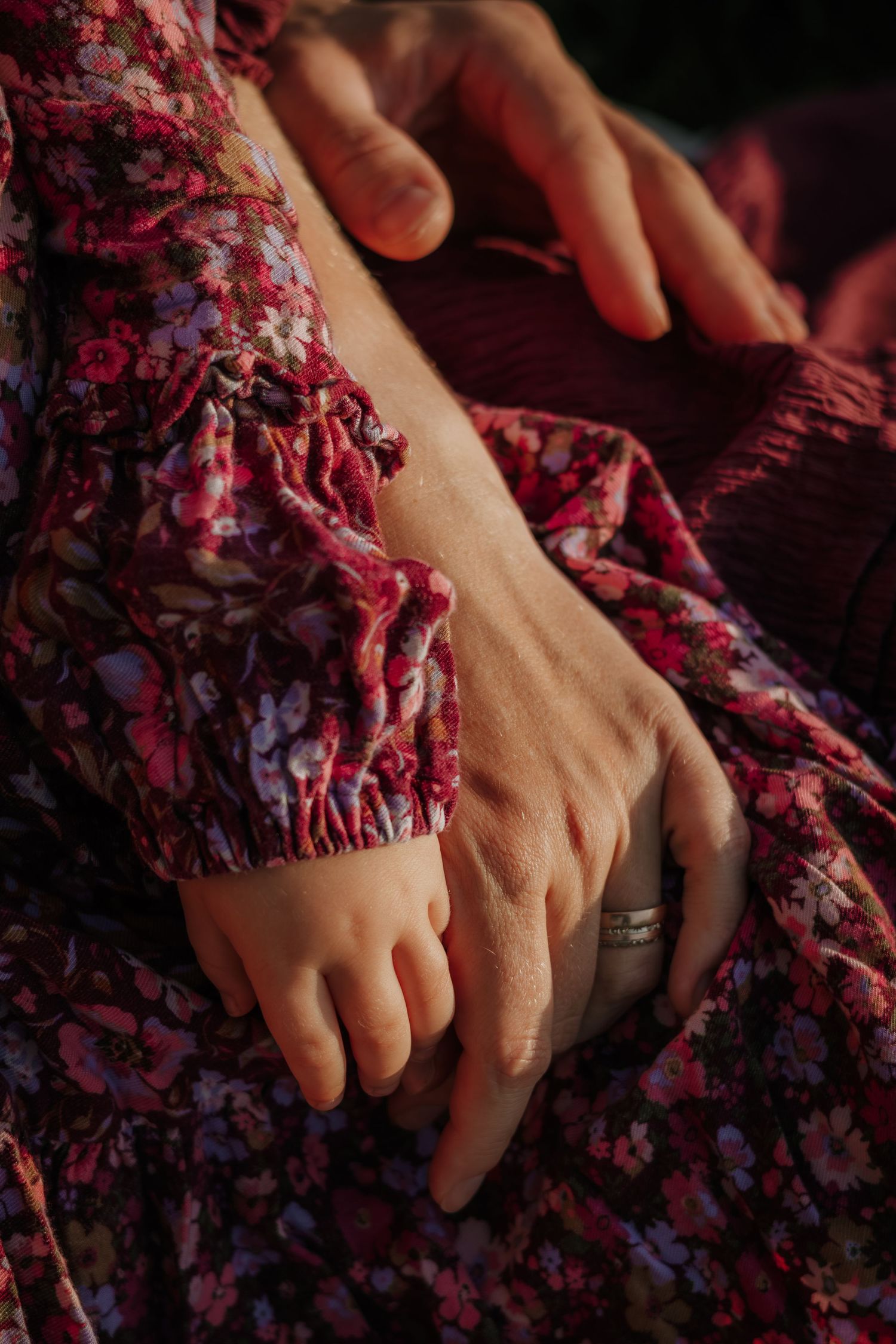 Close-up shot of hands resting on a floral patterned dress in warm lighting.