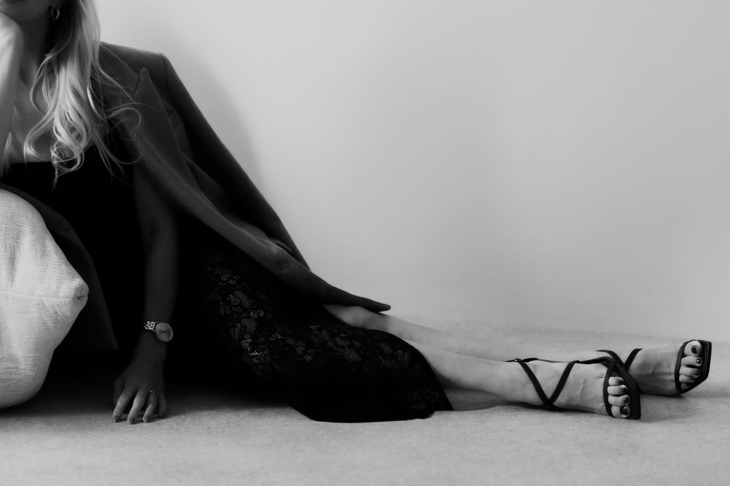 Black and white photo of a woman in a black blazer and lace skirt sitting on the floor wearing Valentino heels.