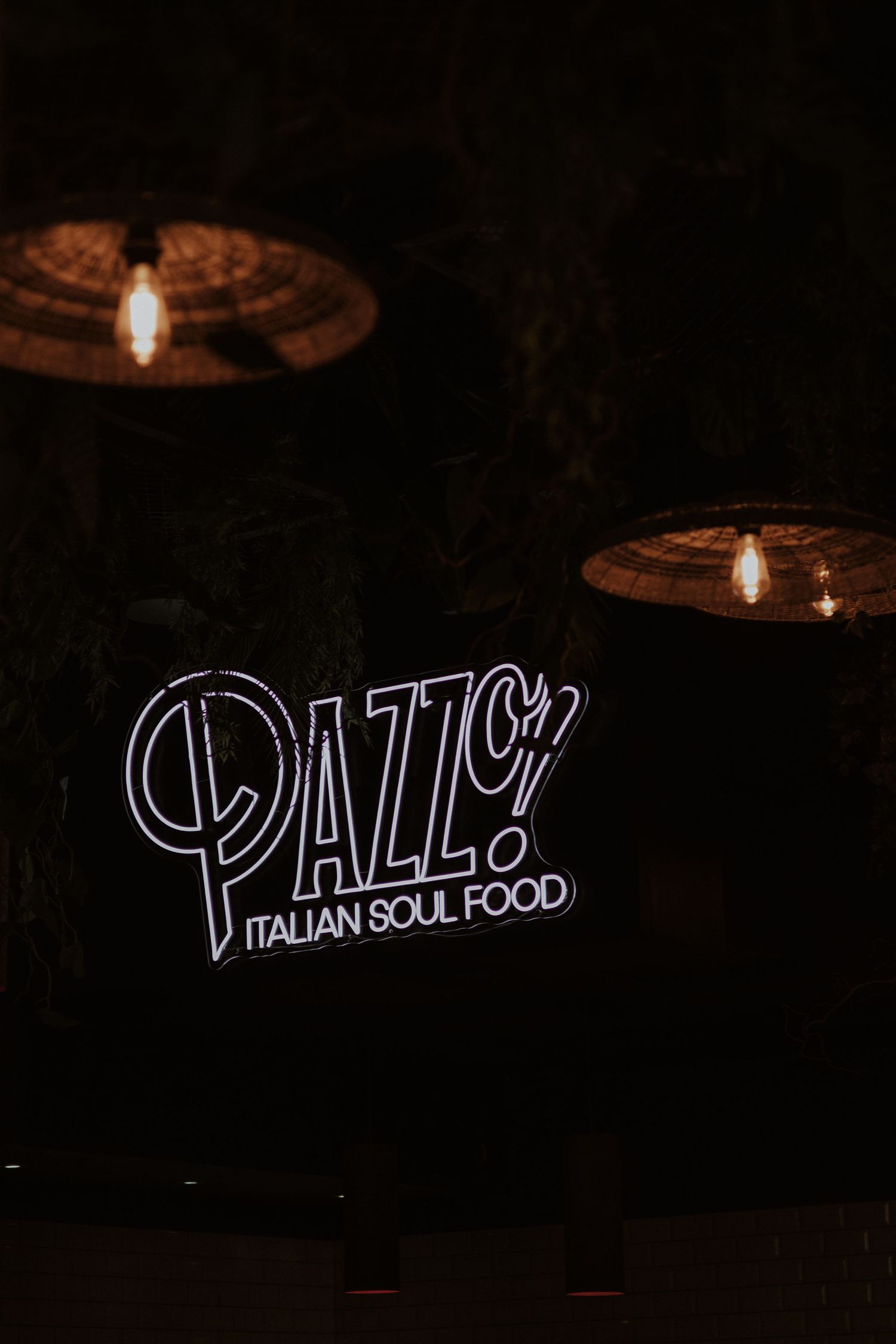 Four illuminated neon signs on dark background displaying restaurant branding for Italian food venue.
