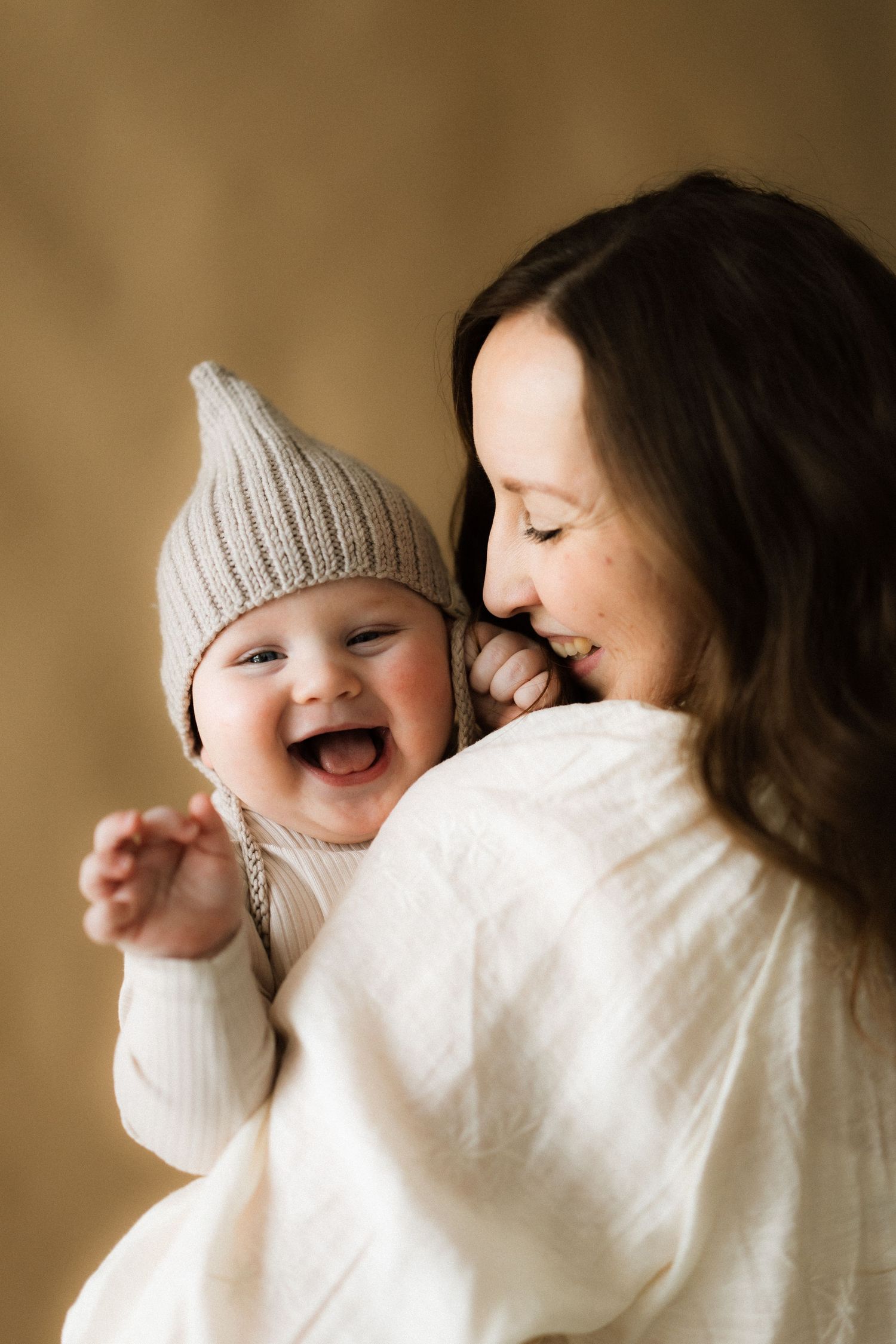 A heartwarming sequence of candid moments between parent and child wearing white sweaters against a warm brown background.