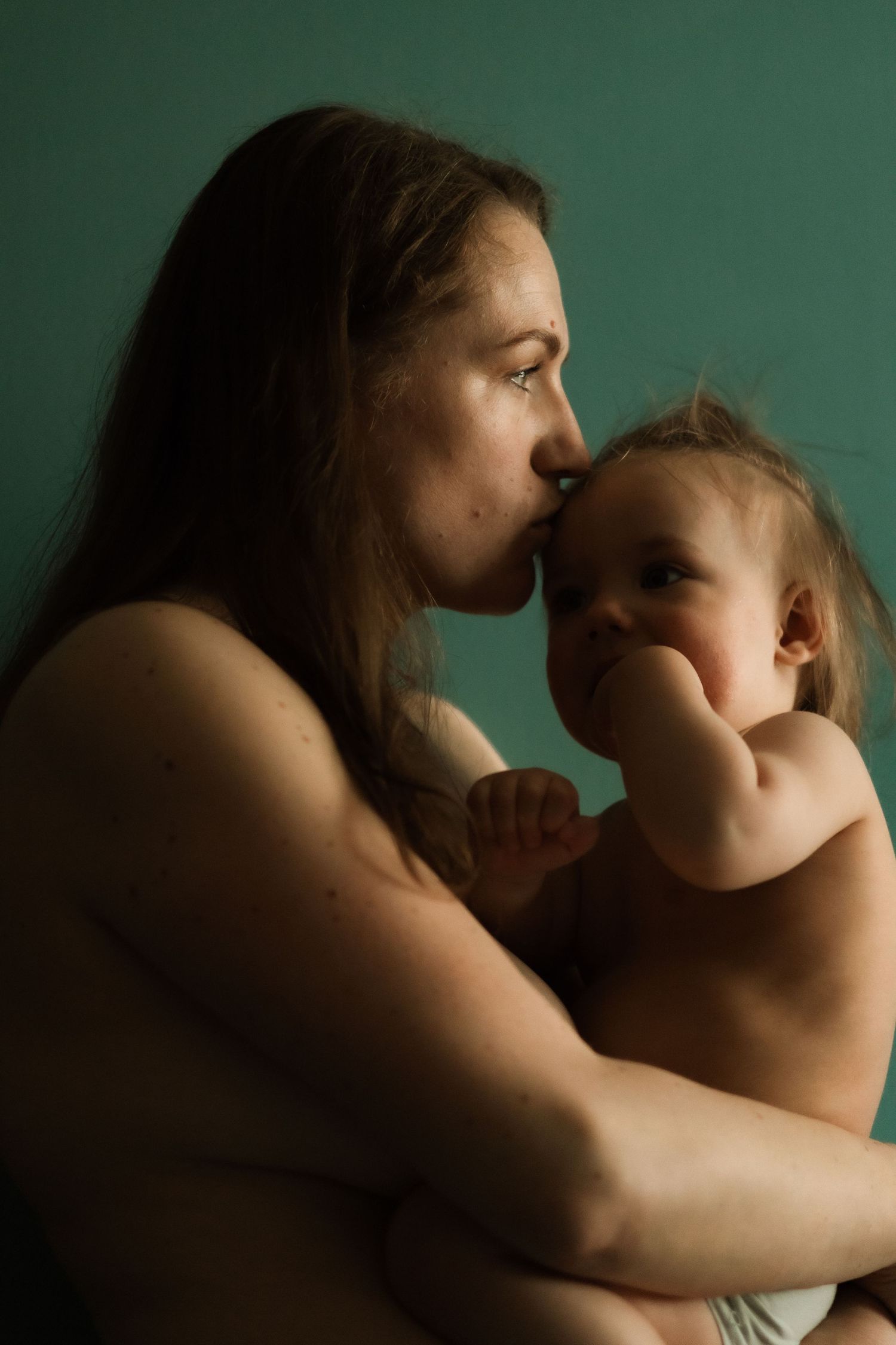 A tender moment between parent and baby captured in moody lighting against a green background.