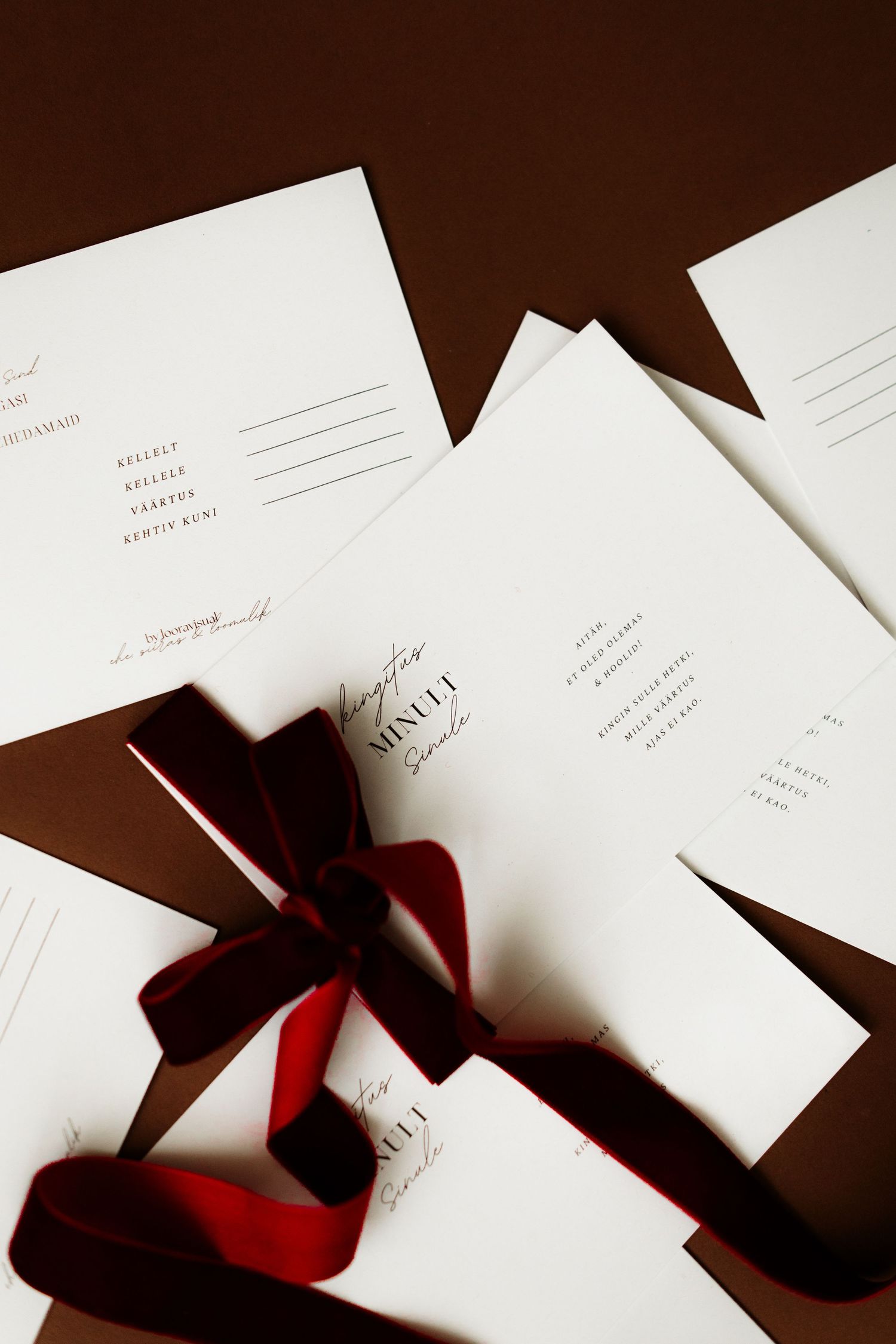 Scattered white wedding invitation cards with elegant red ribbons cast dramatic shadows on a dark brown surface.