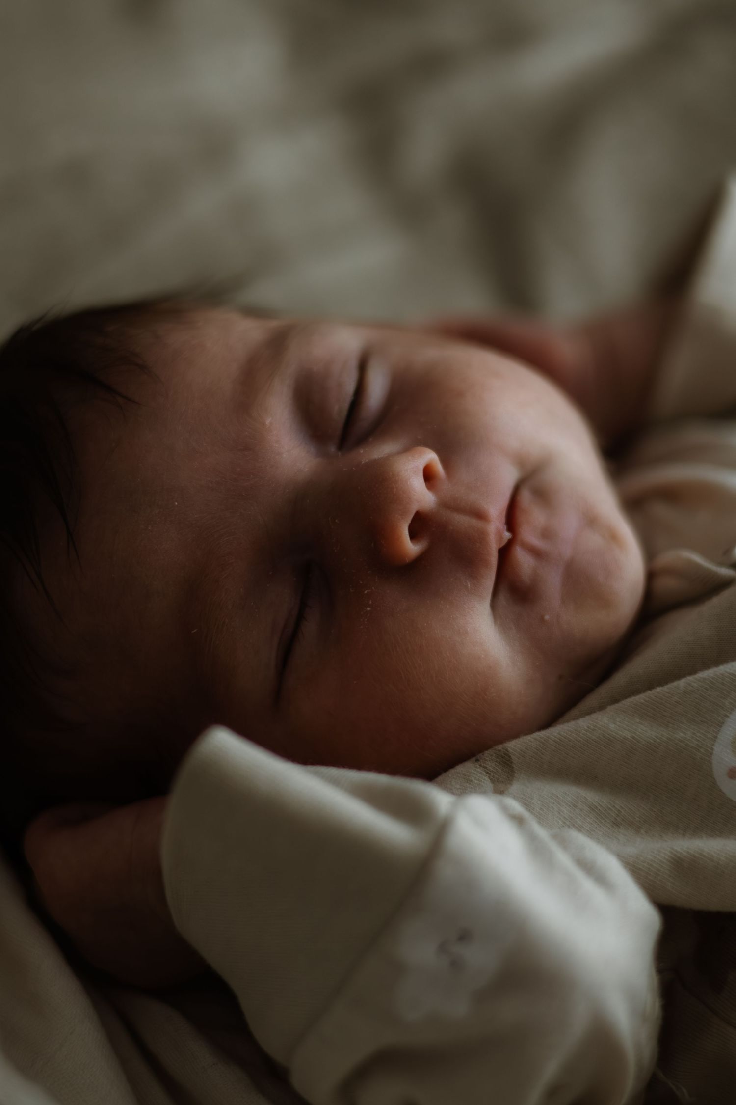 A sleeping baby rests peacefully on white bedding in soft, natural lighting.