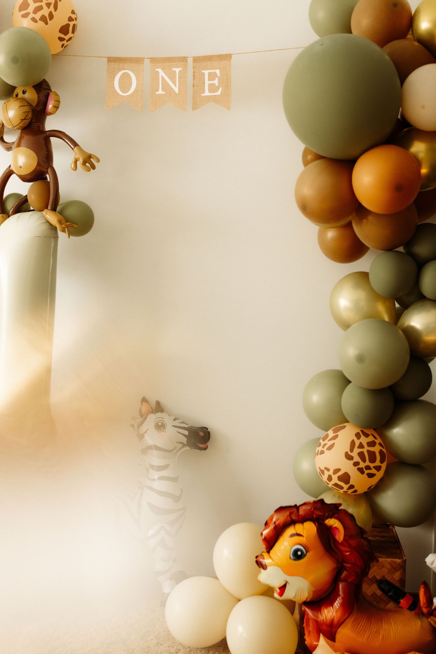 Safari-themed party decorations with brown, sage green and white balloon garland and plush animal accents.