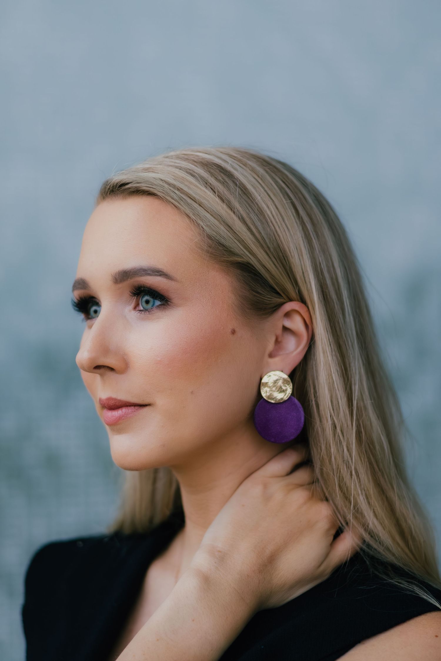 Fashion portrait showing artistic profile angles with statement earrings and elegant makeup against blue backdrop.