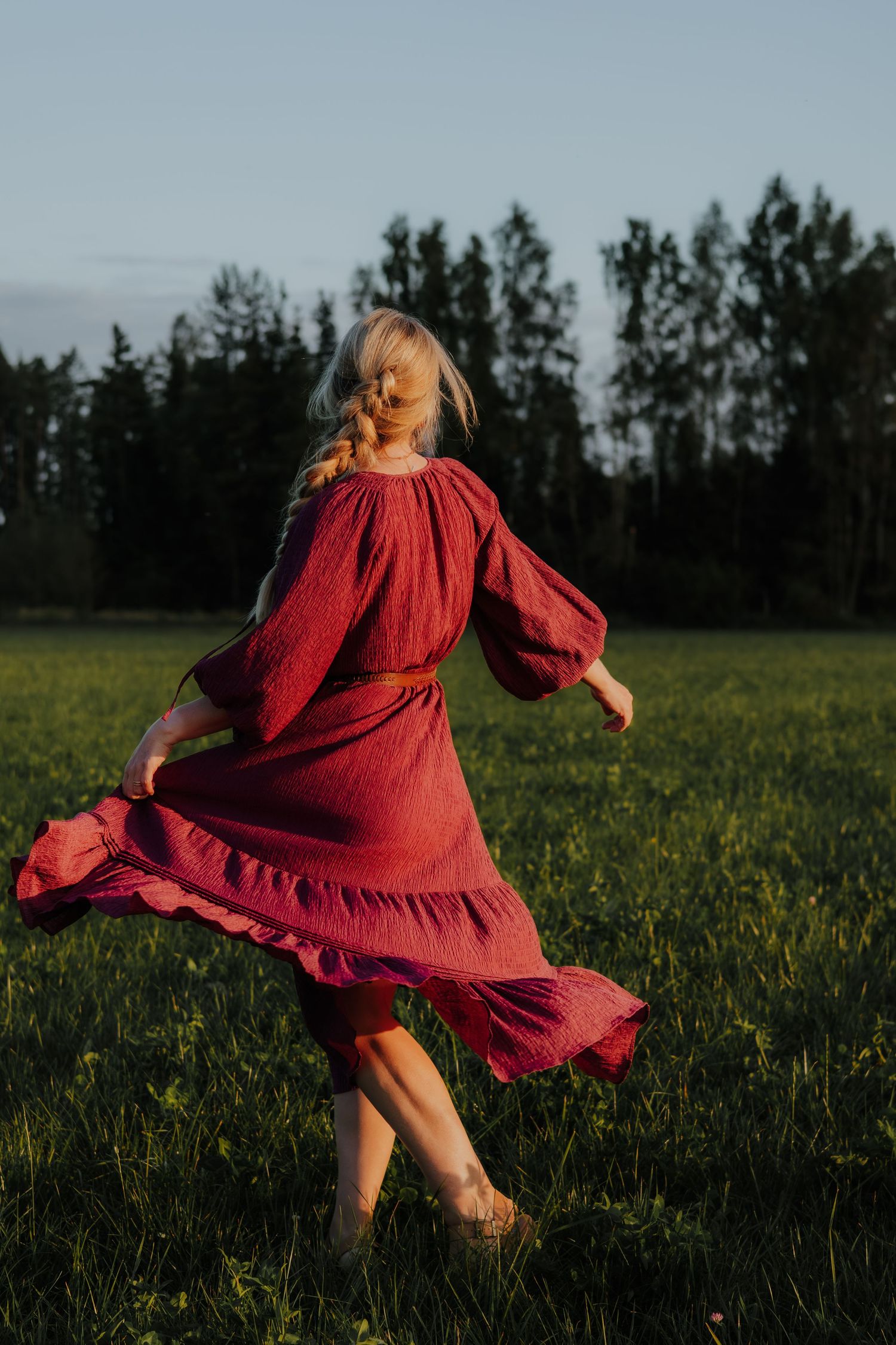 A person in a flowing red dress twirls gracefully in a sunlit meadow filled with wildflowers at dusk.