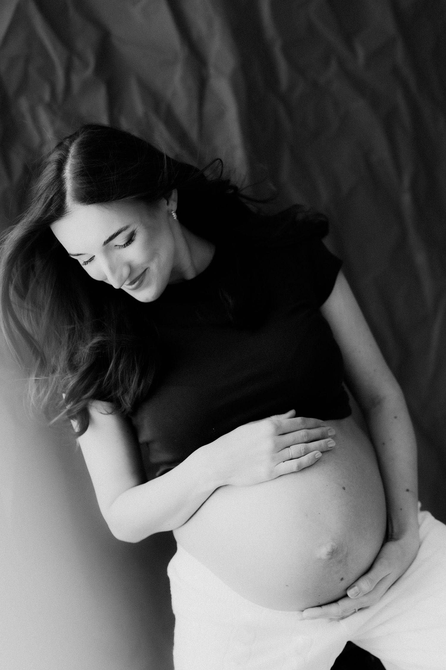 A series of black and white maternity photos showing a pregnant woman's belly in artistic poses against a dark background.