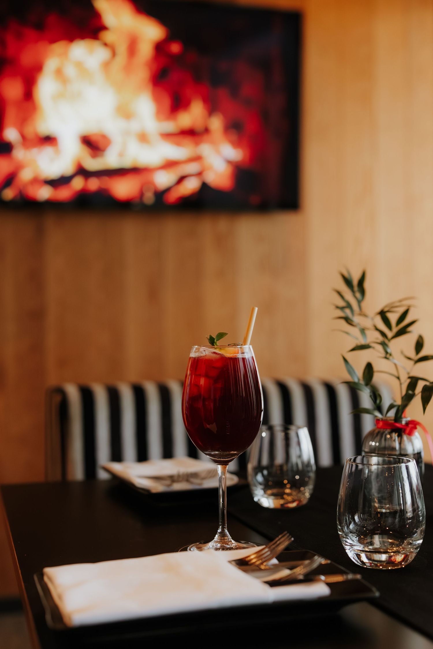 Red cocktail in wine glass on dark table with cozy fireplace display and elegant table setting in restaurant atmosphere.