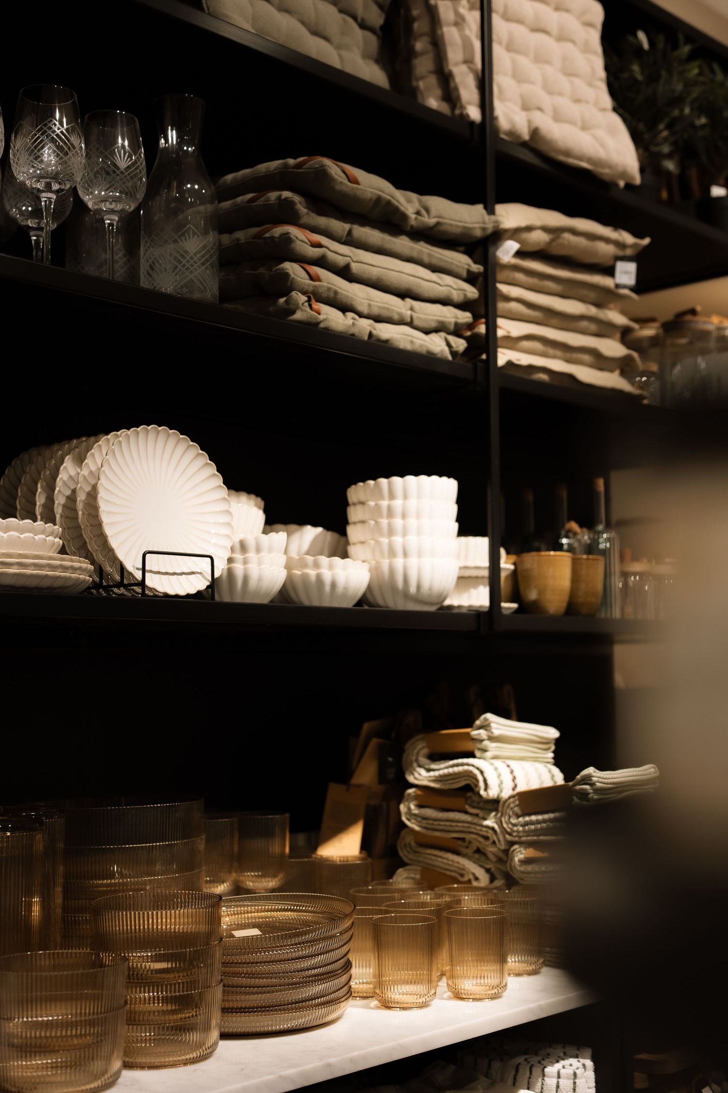 Rustic shelves display vintage glassware, white ceramic dishes, and neatly folded linens in warm ambient lighting.