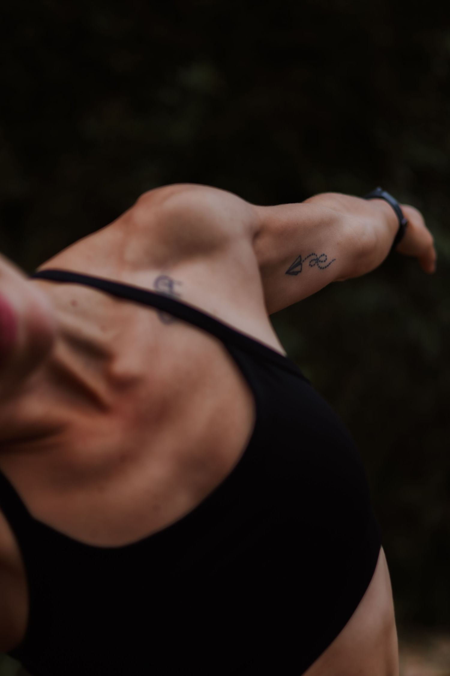 Close-up of a person wearing a black sports bra with a small tattoo visible on their shoulder in dark lighting.