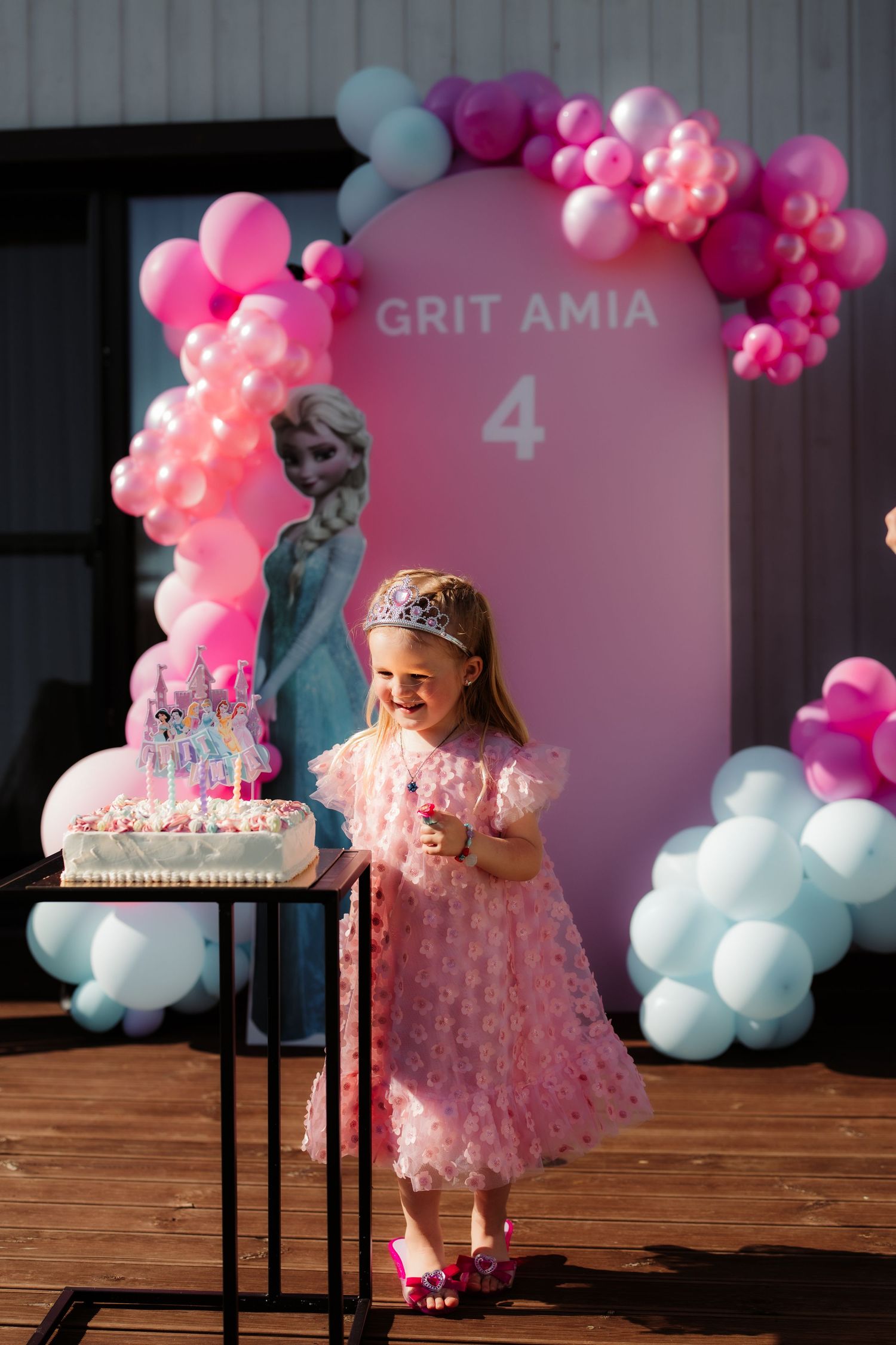 Girl in pink dress celebrates 4th birthday with cake and balloon arch at Grit Amia themed party.