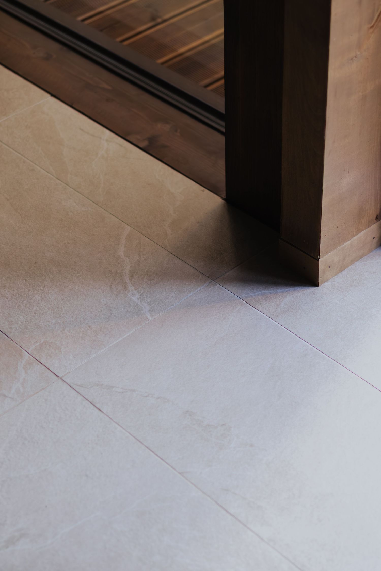 White porcelain floor tiles with subtle grey veining pattern and dark wooden door trim visible in corner.