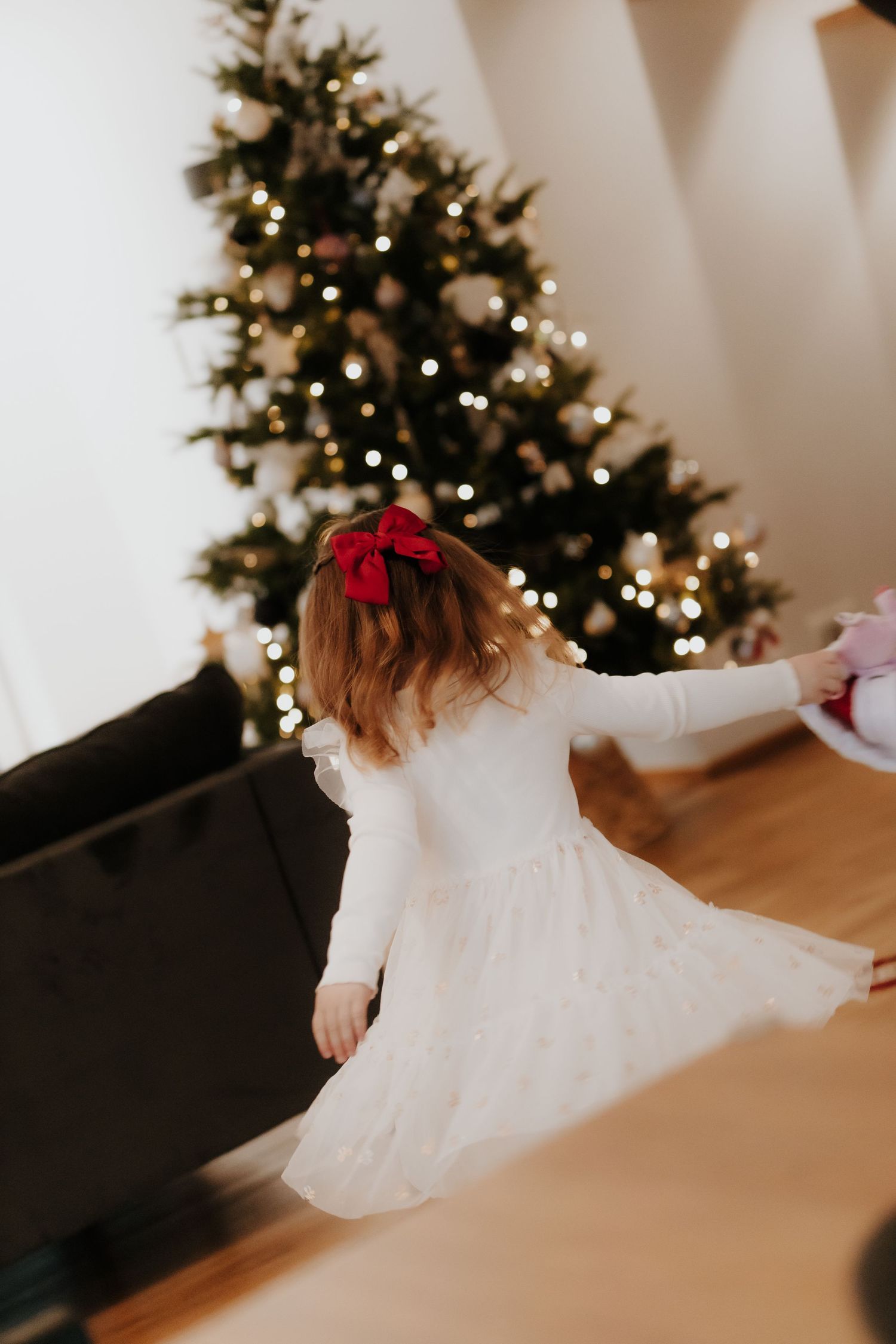 A child in a white dress twirls and spins in front of a decorated Christmas tree with twinkling lights.