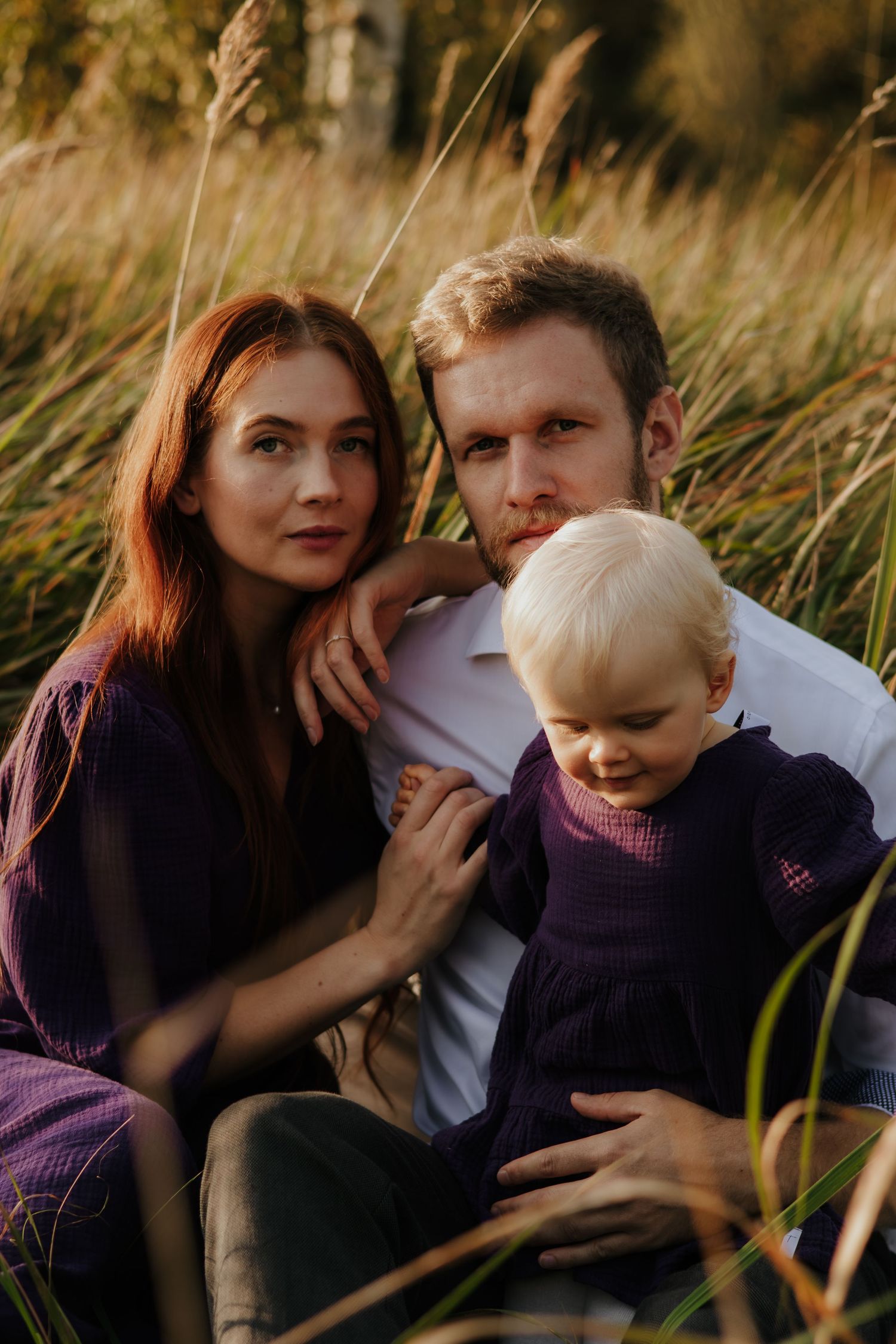 A family shares tender moments together while sitting in tall grass during golden hour.