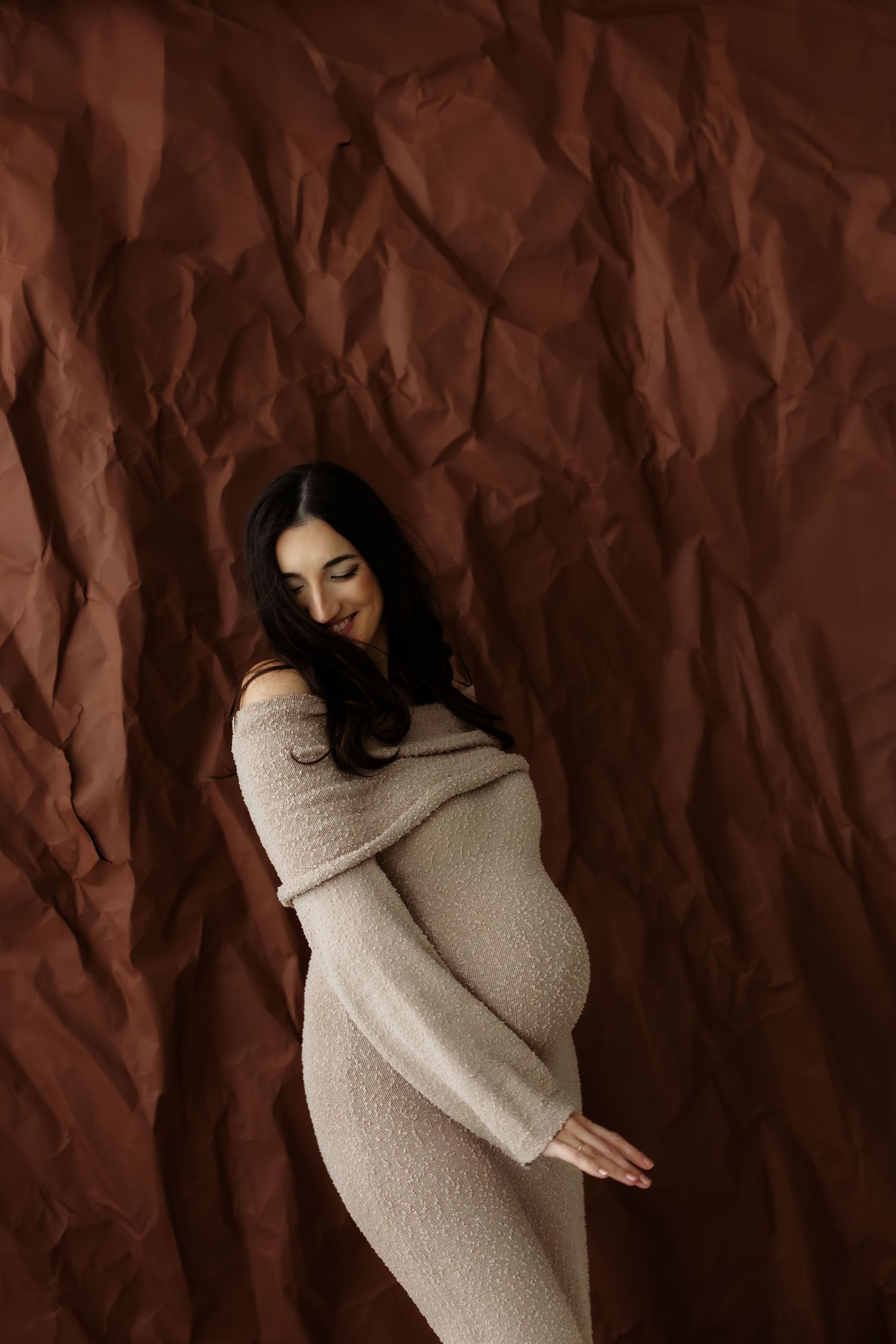 Figure in cozy beige sweater poses against textured brown backdrop in artistic portrait series.