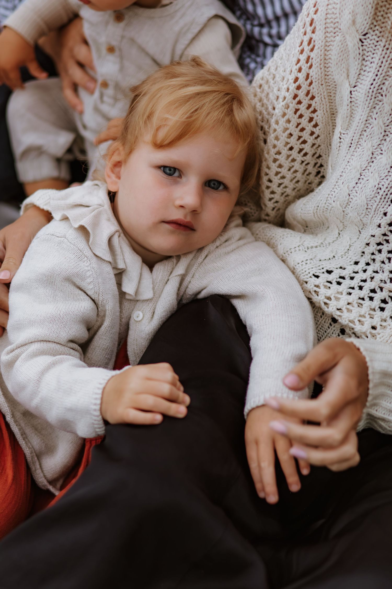 A small child in a white sweater rests against cozy knit fabrics and dark textiles in a series of candid moments.