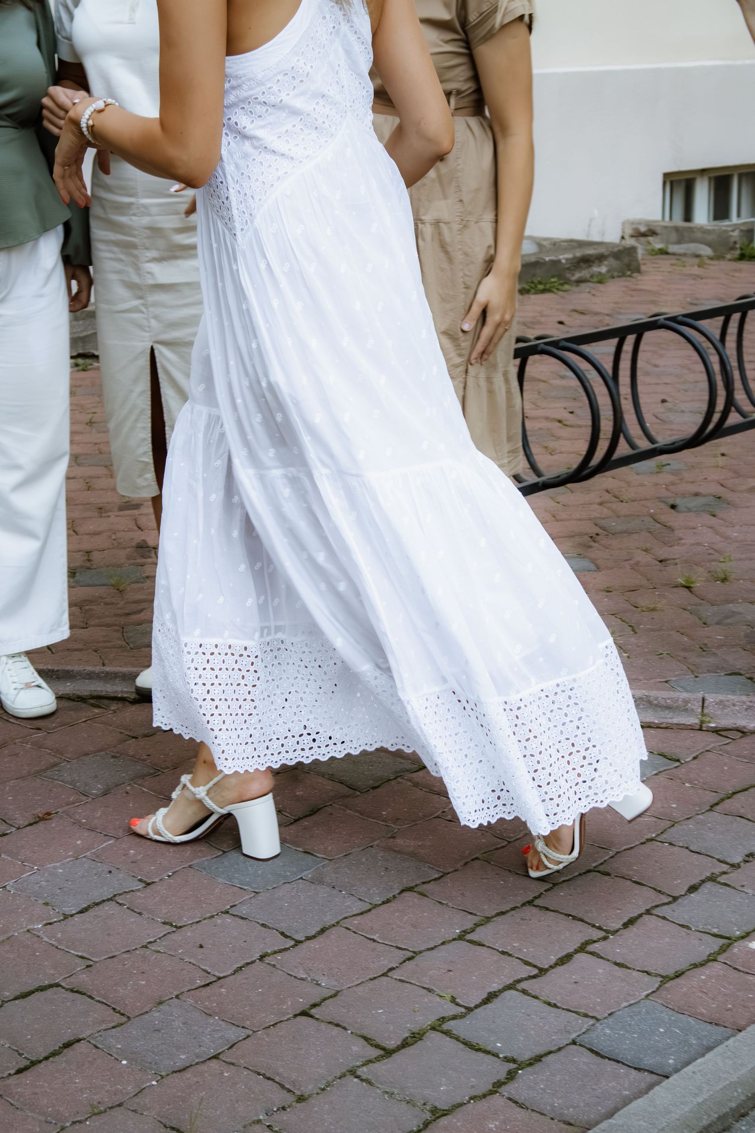 Close-up view of white eyelet lace dress hem and sandals on brick patio during outdoor event.