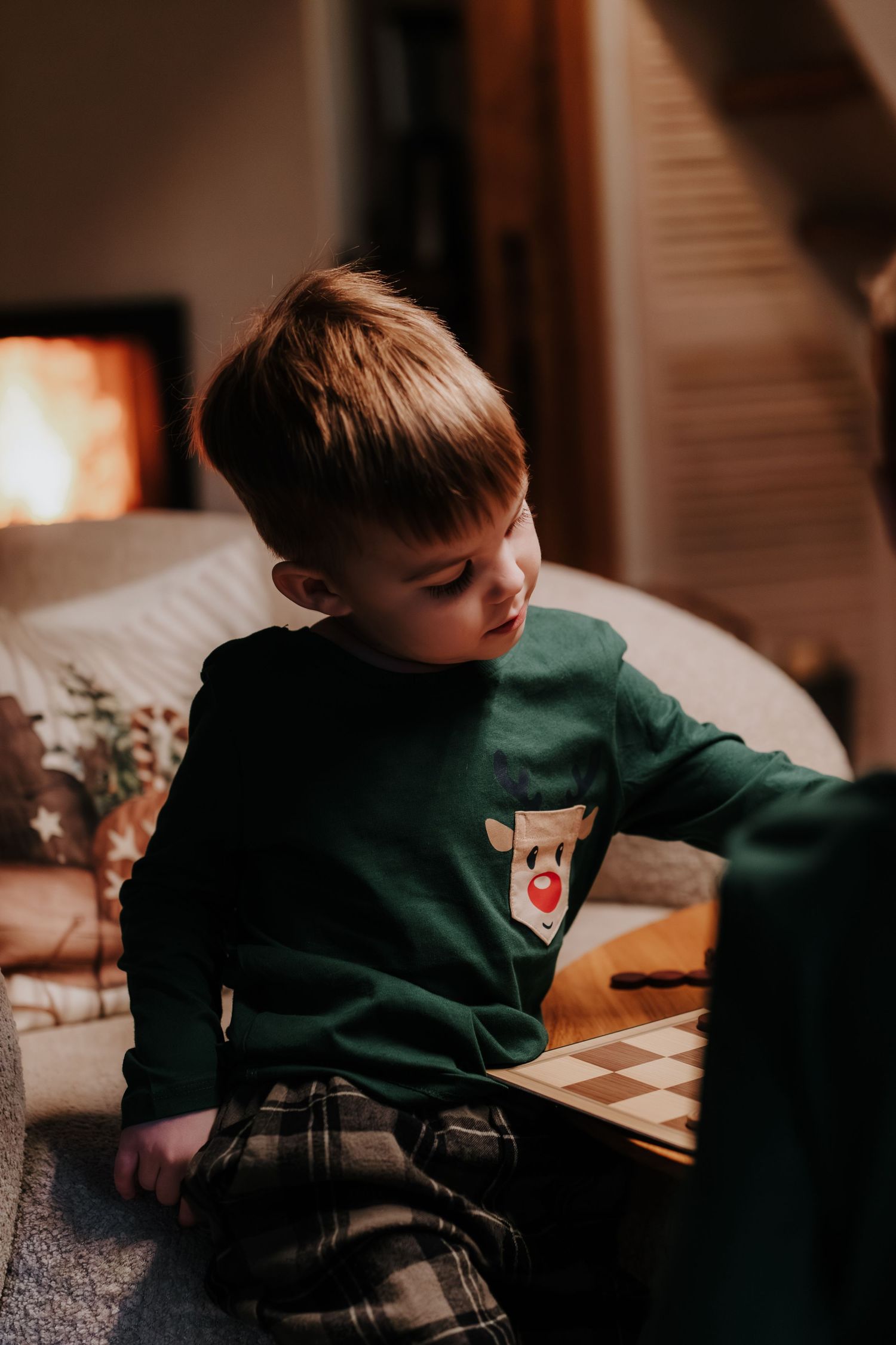 A young child in a green sweater sits at a table doing an activity in a warmly lit room.