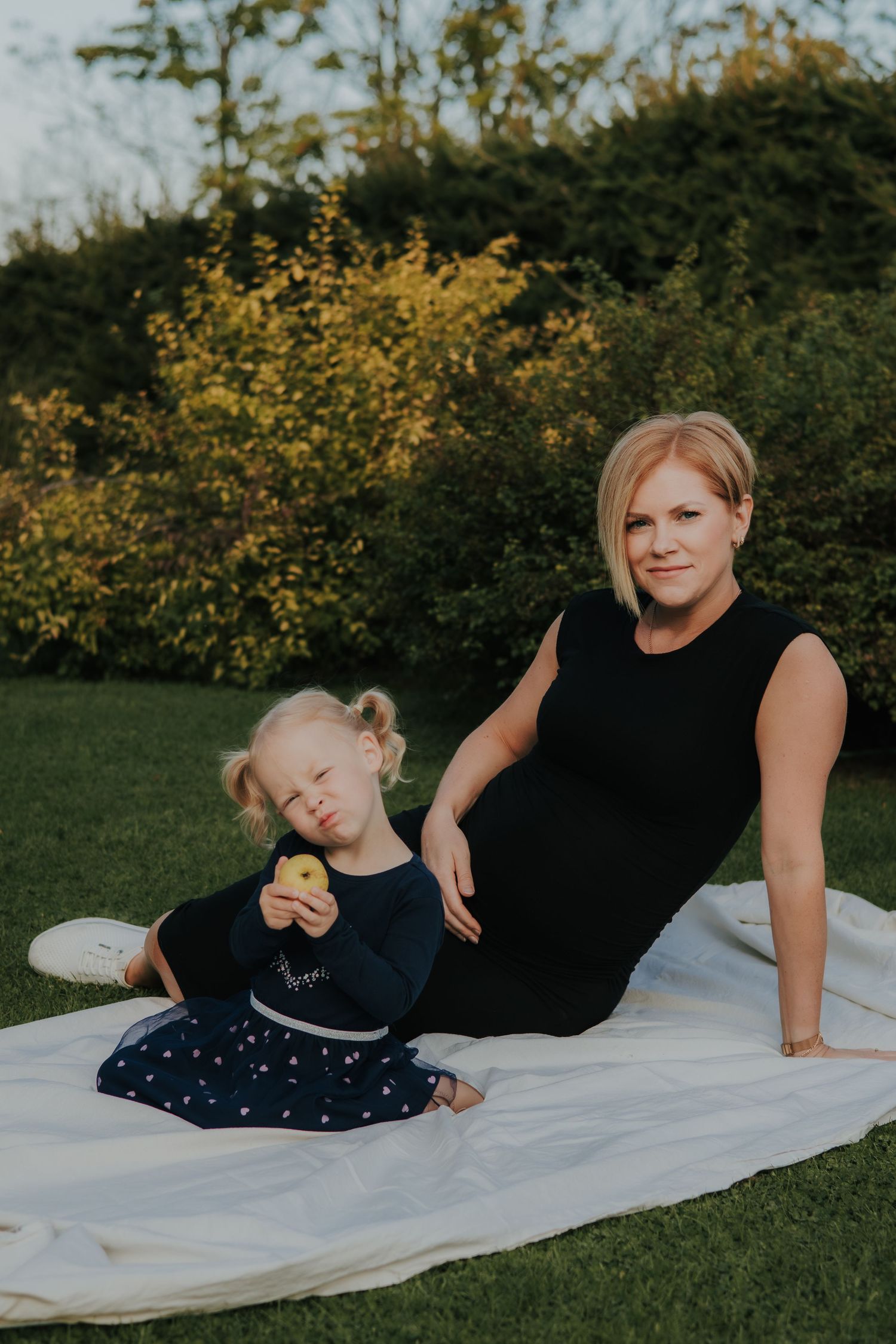 A person in a navy dress relaxes on a white blanket in the grass during a summer photoshoot.